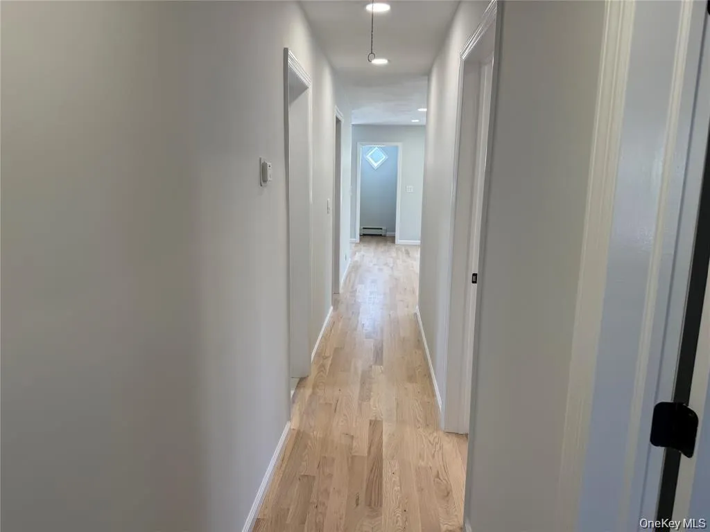 Hallway featuring light wood finished floors, recessed lighting, and a baseboard radiator Hallway featuring light wood finished floors, recessed lighting, and a baseboard radiator