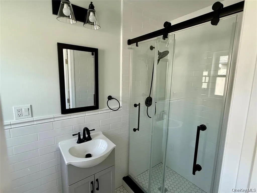 Full bath featuring vanity, tile walls, a shower stall, and a wainscoted wall Full bath featuring vanity, tile walls, a shower stall, and a wainscoted wall
