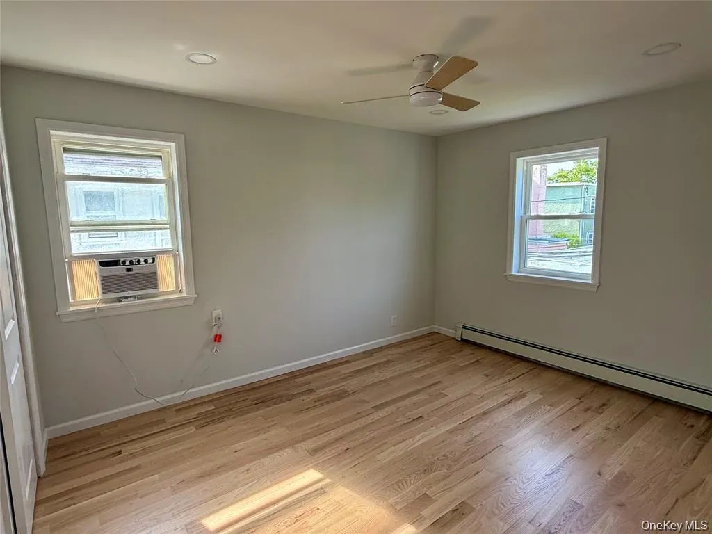 Spare room featuring baseboard heating, light wood finished floors, cooling unit, and a ceiling fan Spare room featuring baseboard heating, light wood finished floors, cooling unit, and a ceiling fan
