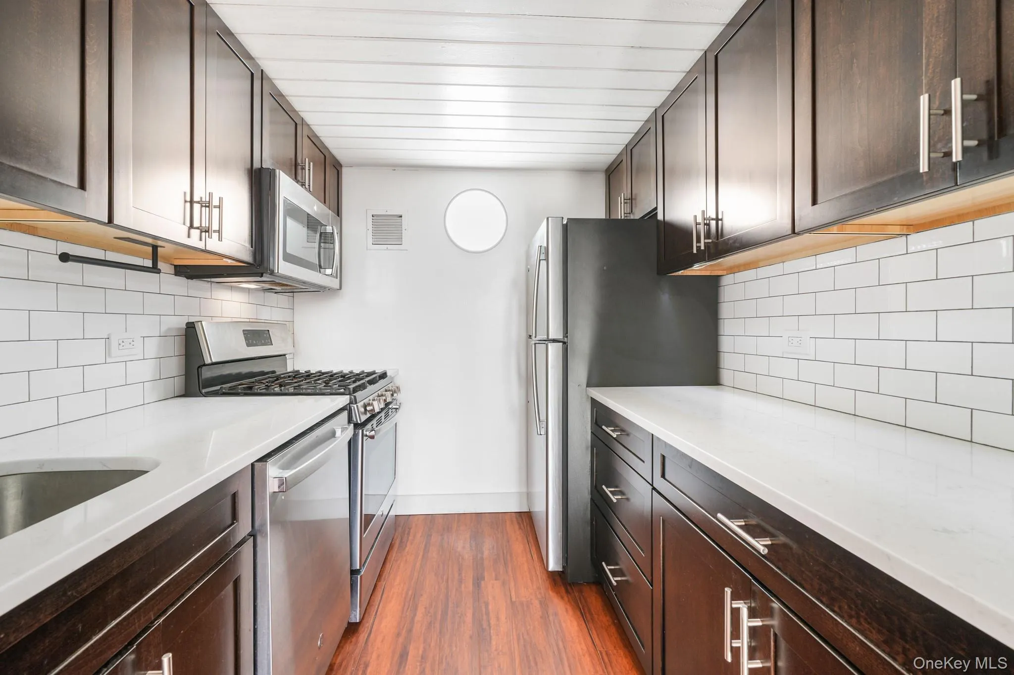 Kitchen with dark brown cabinetry, decorative backsplash, stainless steel appliances, and dark wood-style flooring Kitchen with dark brown cabinetry, decorative backsplash, stainless steel appliances, and dark wood-style flooring