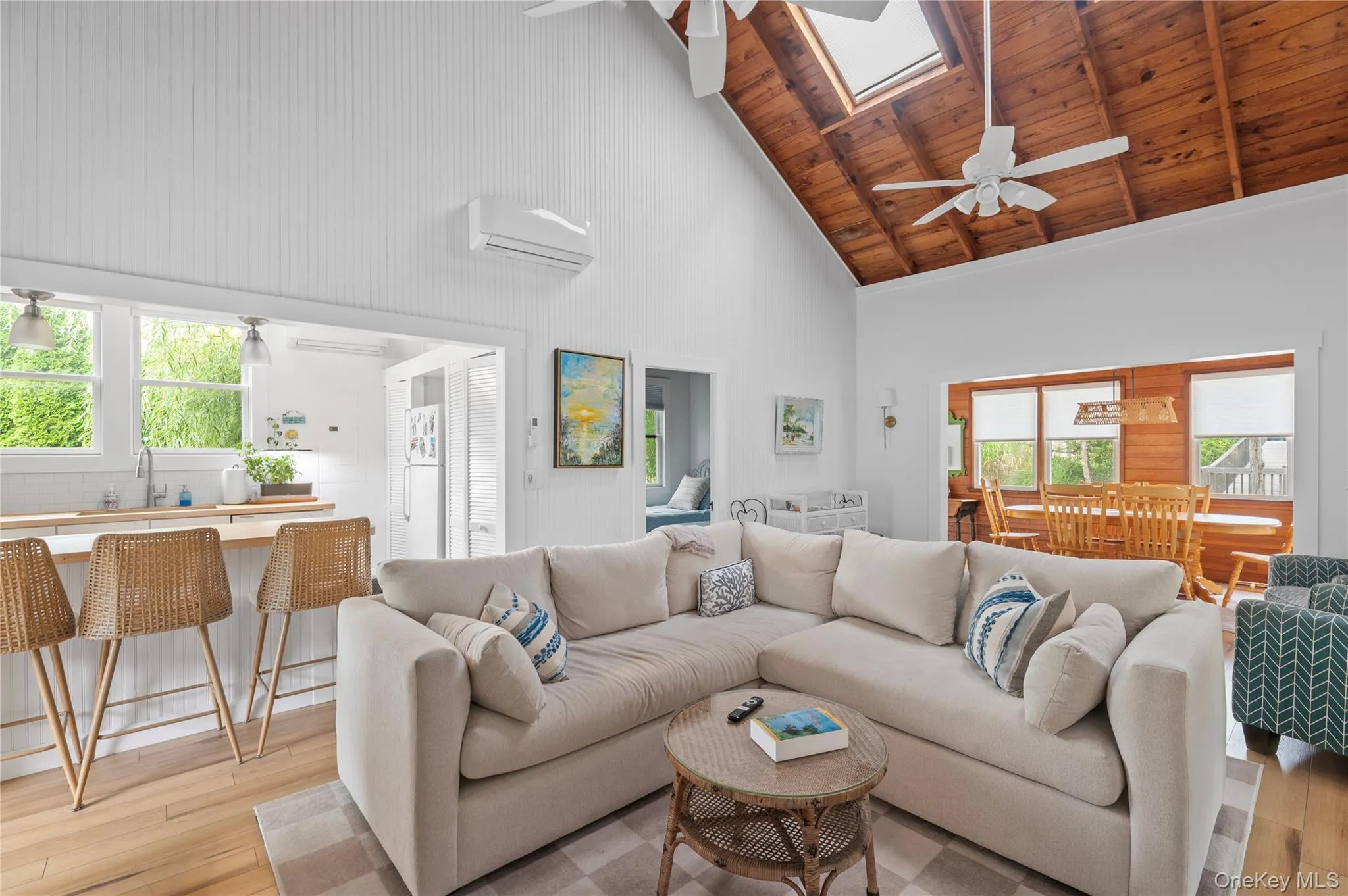 Living area with a ceiling fan, high vaulted ceiling, light wood-type flooring, an AC wall unit, and a skylight Living area with a ceiling fan, high vaulted ceiling, light wood-type flooring, an AC wall unit, and a skylight
