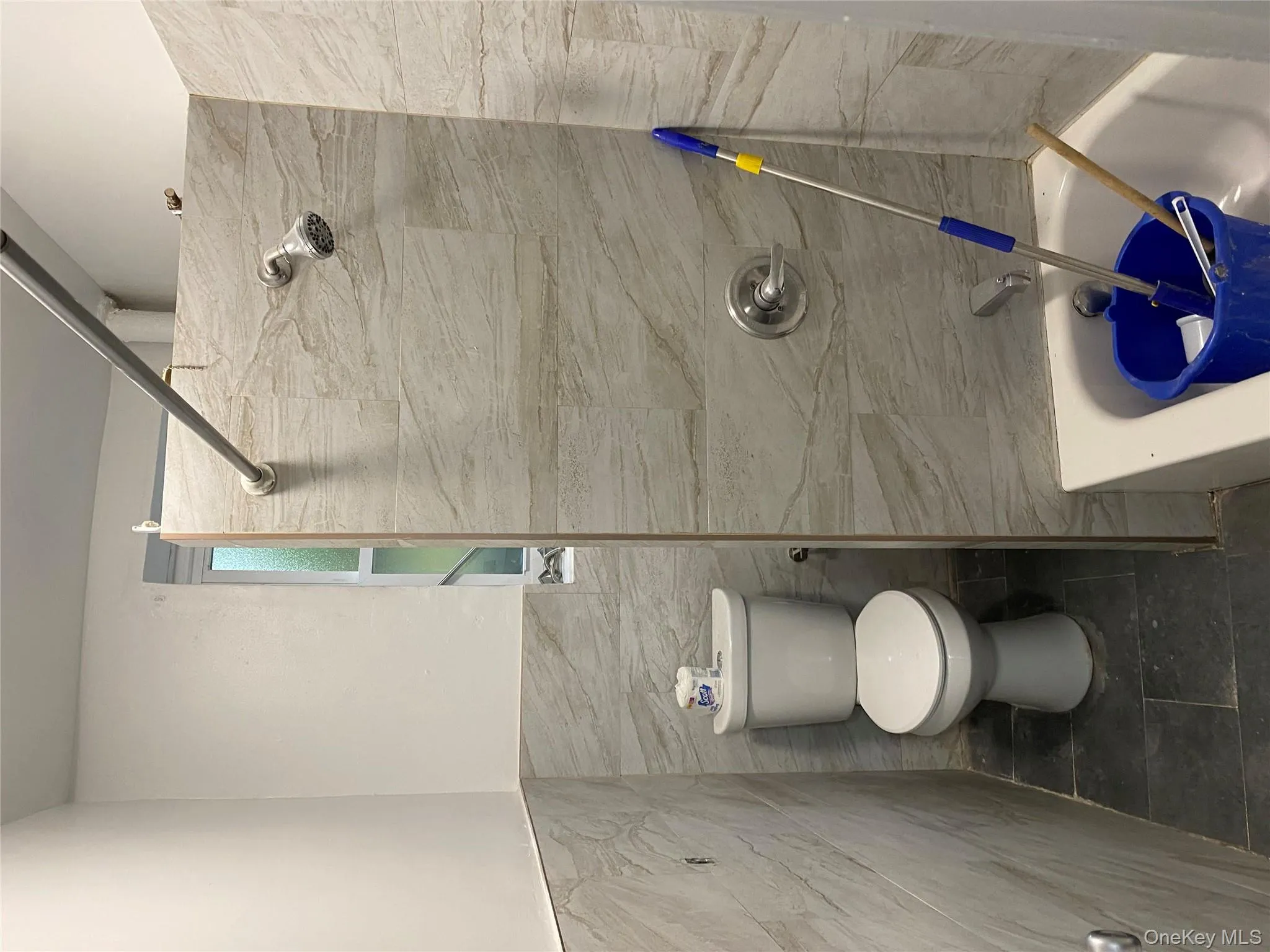 Full bath with tile walls, shower / bathtub combination, dark tile patterned flooring, and a wainscoted wall Full bath with tile walls, shower / bathtub combination, dark tile patterned flooring, and a wainscoted wall