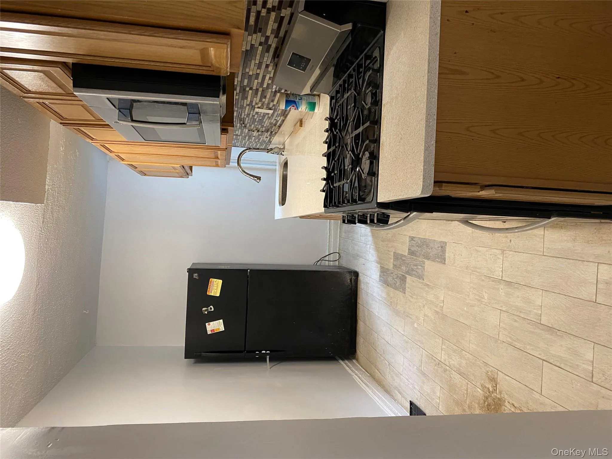 Kitchen with stainless steel stove, decorative backsplash, freestanding refrigerator, a textured ceiling, and wood tiled floors Kitchen with stainless steel stove, decorative backsplash, freestanding refrigerator, a textured ceiling, and wood tiled floors