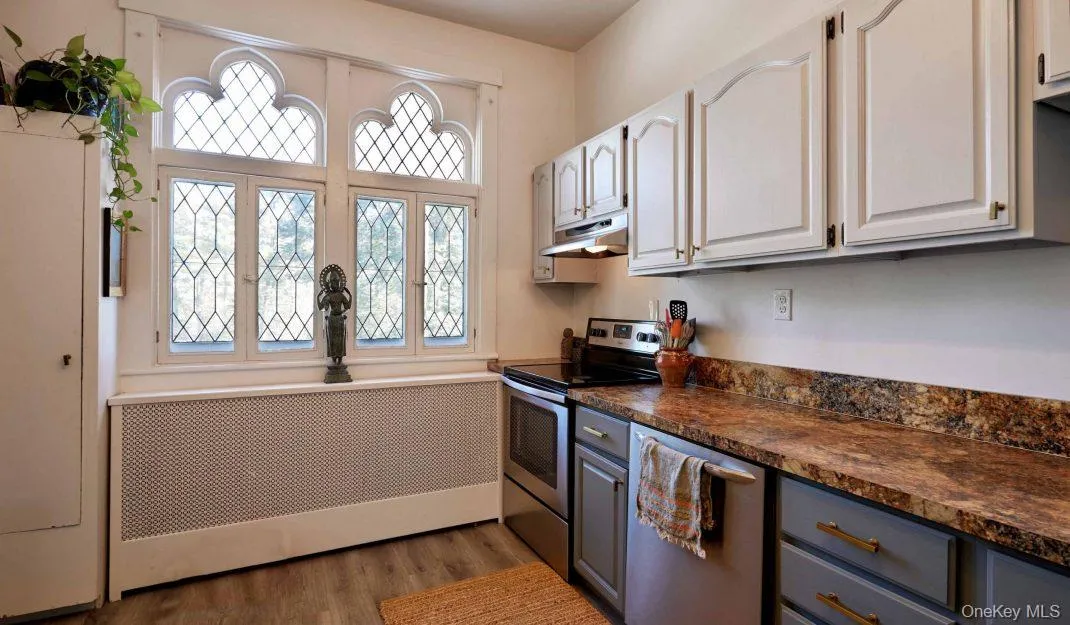 Kitchen featuring dark countertops, radiator heating unit, stainless steel appliances, light wood finished floors, and wainscoting Kitchen featuring dark countertops, radiator heating unit, stainless steel appliances, light wood finished floors, and wainscoting