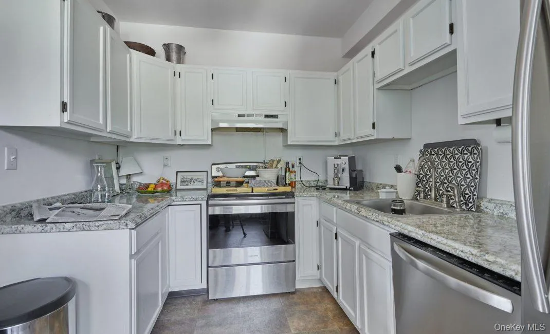 Kitchen featuring appliances with stainless steel finishes, white cabinets, light countertops, under cabinet range hood, and stone finish flooring Kitchen featuring appliances with stainless steel finishes, white cabinets, light countertops, under cabinet range hood, and stone finish flooring