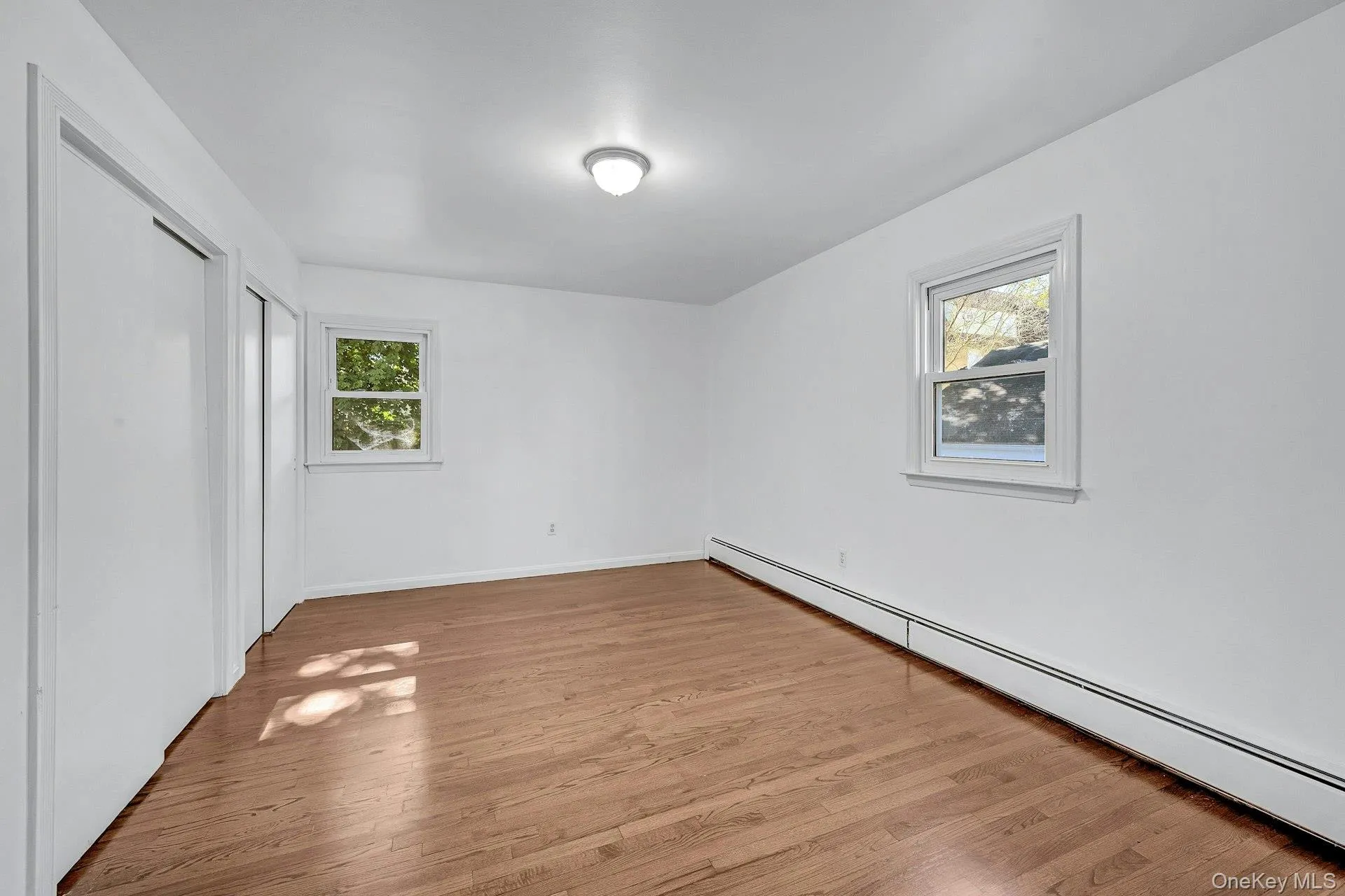 Unfurnished bedroom featuring a baseboard heating unit, light wood-style floors, and a closet Unfurnished bedroom featuring a baseboard heating unit, light wood-style floors, and a closet