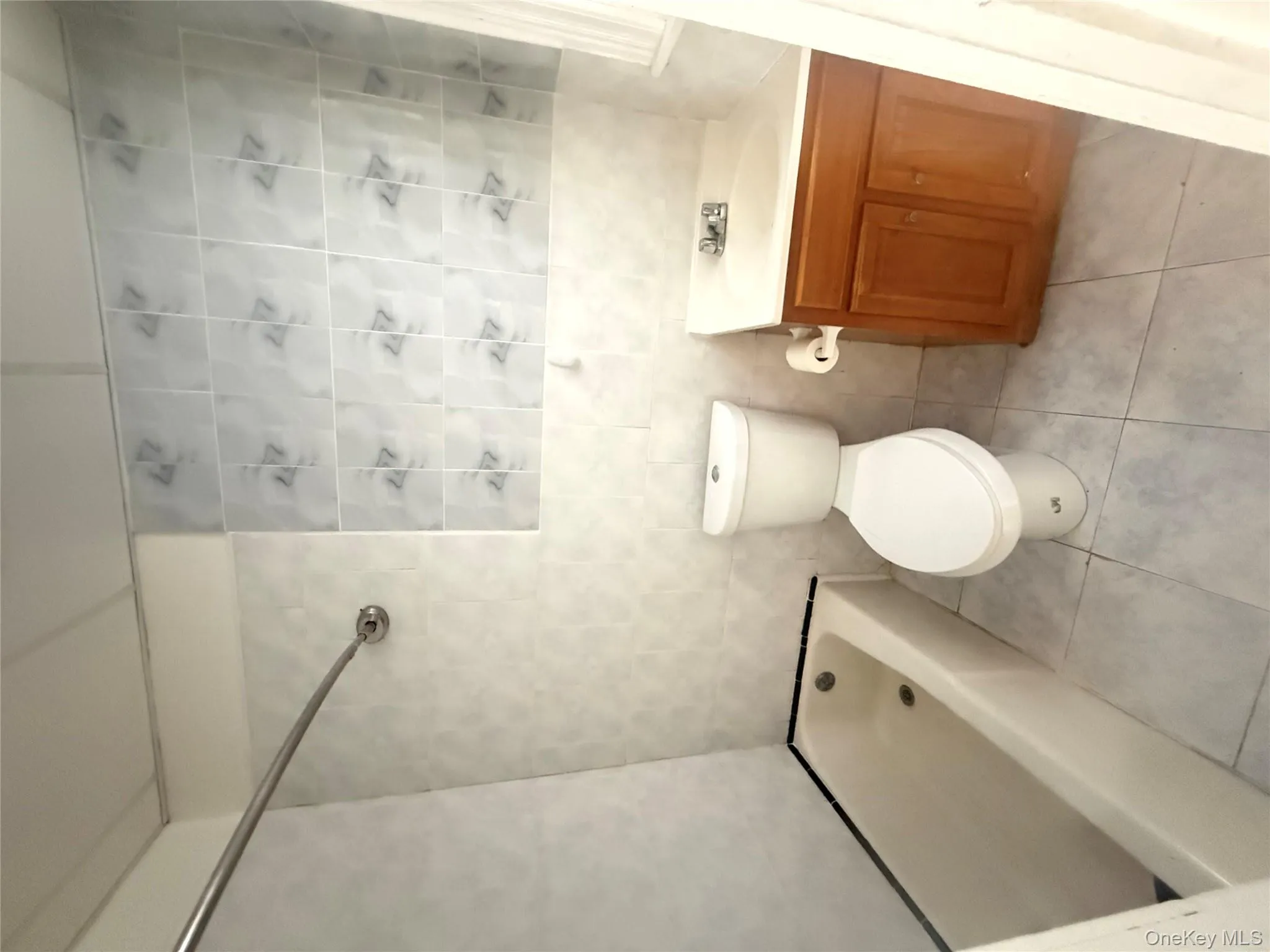 Bathroom with tile walls, vanity, washtub / shower combination, and light tile patterned floors Bathroom with tile walls, vanity, washtub / shower combination, and light tile patterned floors