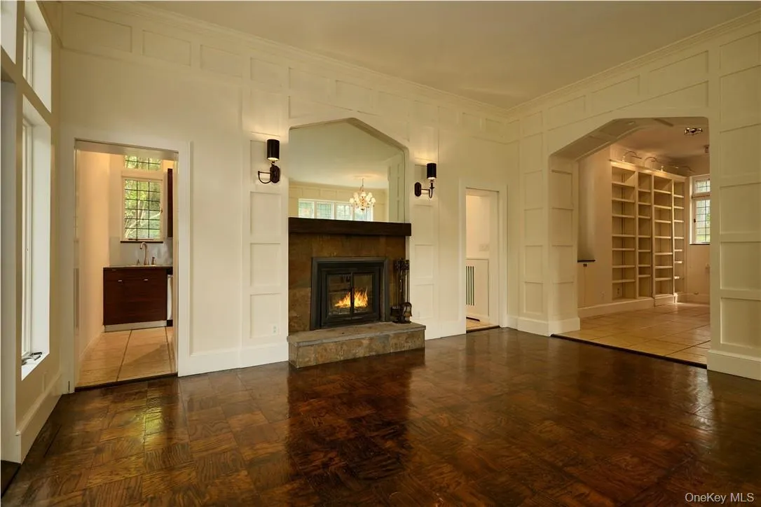 Unfurnished living room with a notable chandelier, built in shelves, and dark tile flooring Unfurnished living room with a notable chandelier, built in shelves, and dark tile flooring