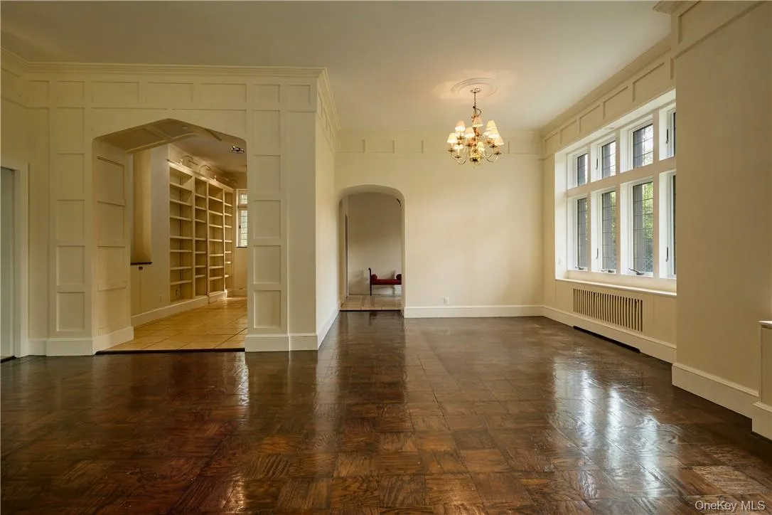 Empty room with a notable chandelier, parquet flooring, radiator, and ornamental molding Empty room with a notable chandelier, parquet flooring, radiator, and ornamental molding
