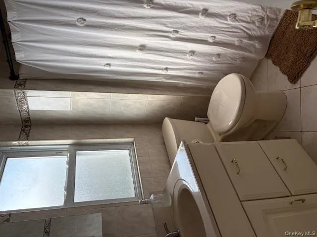 Full bath featuring tile walls, vanity, light tile patterned floors, and a shower with shower curtain Full bath featuring tile walls, vanity, light tile patterned floors, and a shower with shower curtain
