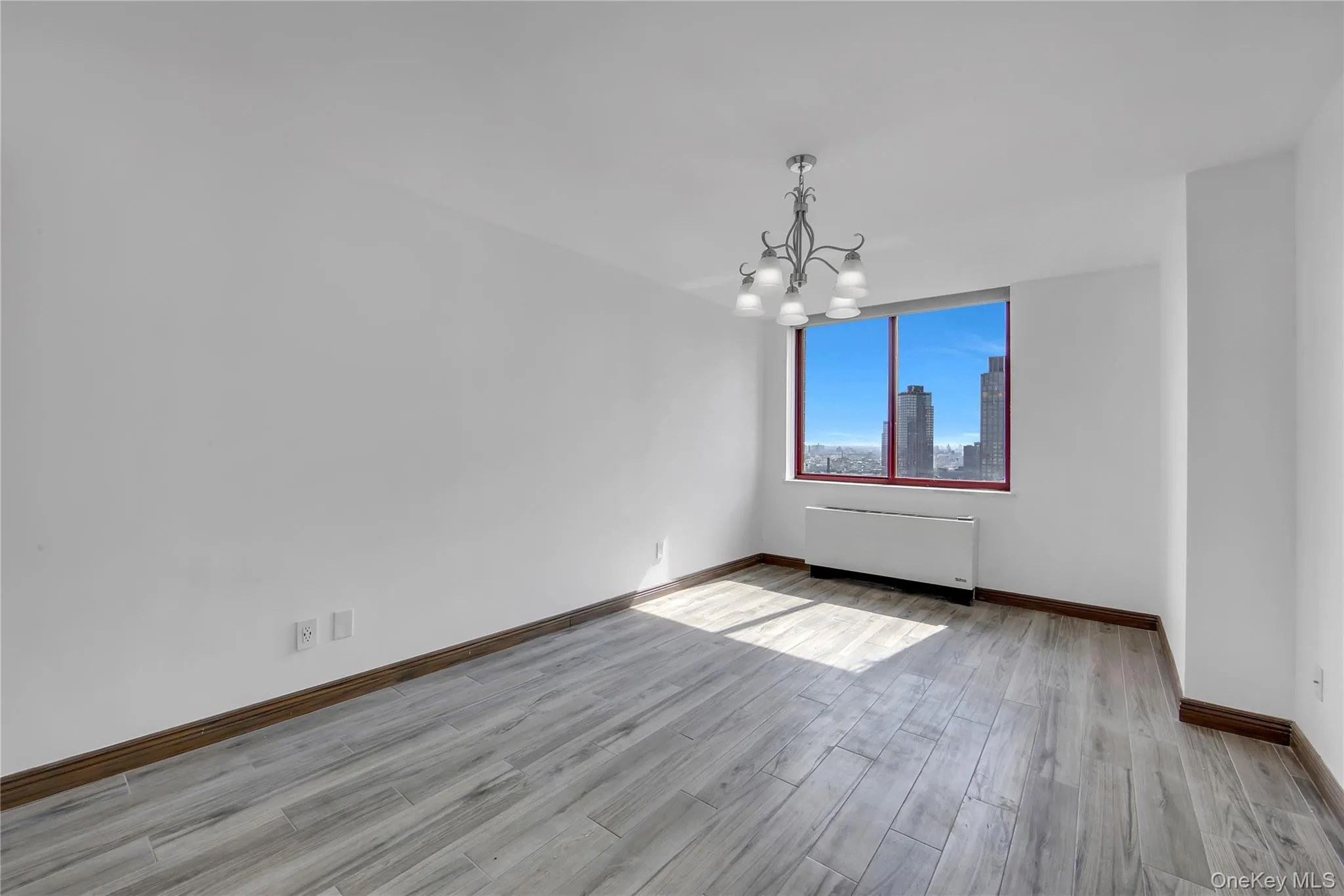Unfurnished dining area featuring radiator, a chandelier, light wood finished floors, and a skyline view Unfurnished dining area featuring radiator, a chandelier, light wood finished floors, and a skyline view
