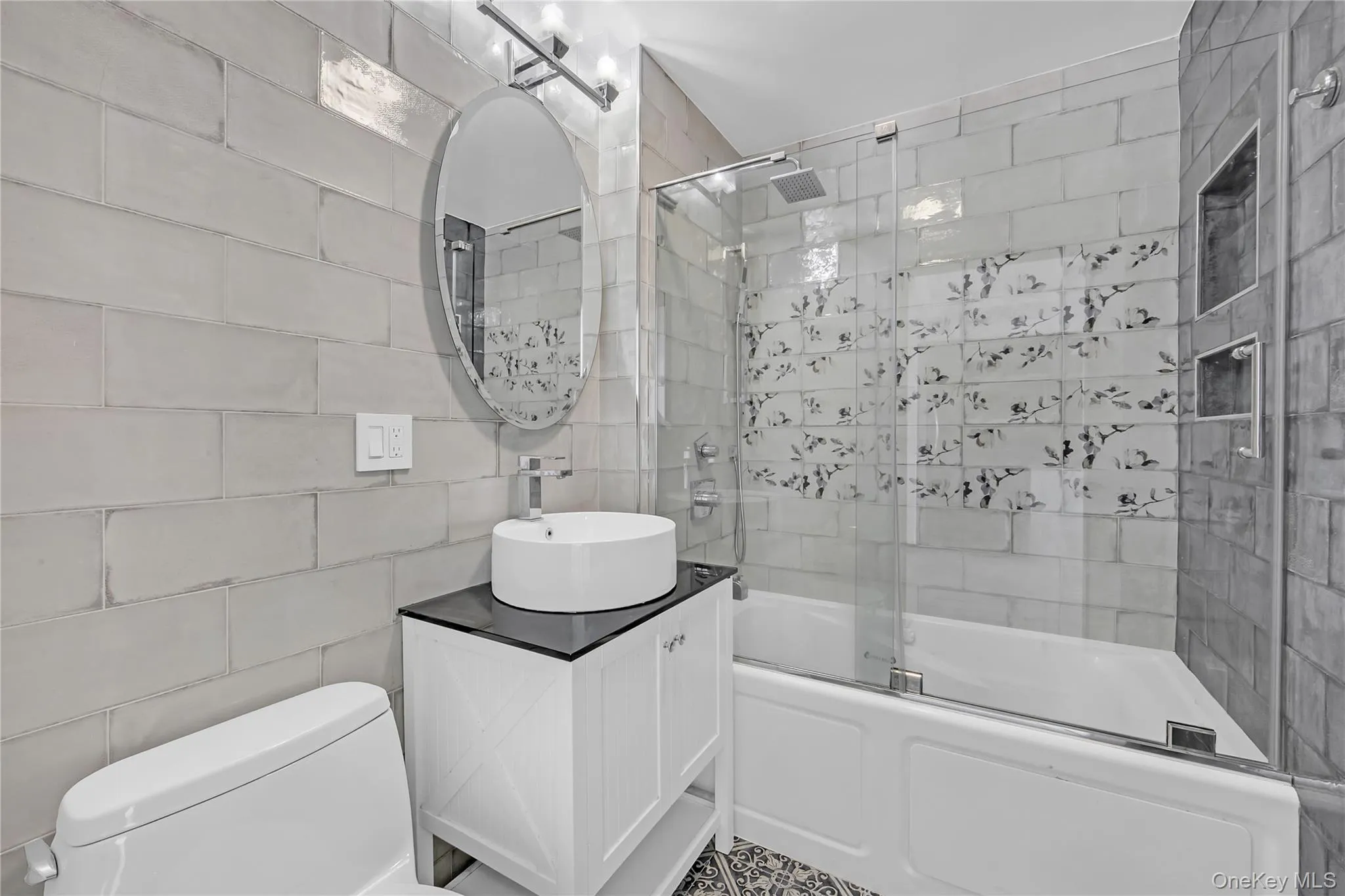 Bathroom featuring vanity, shower / bath combination with glass door, and tile walls Bathroom featuring vanity, shower / bath combination with glass door, and tile walls