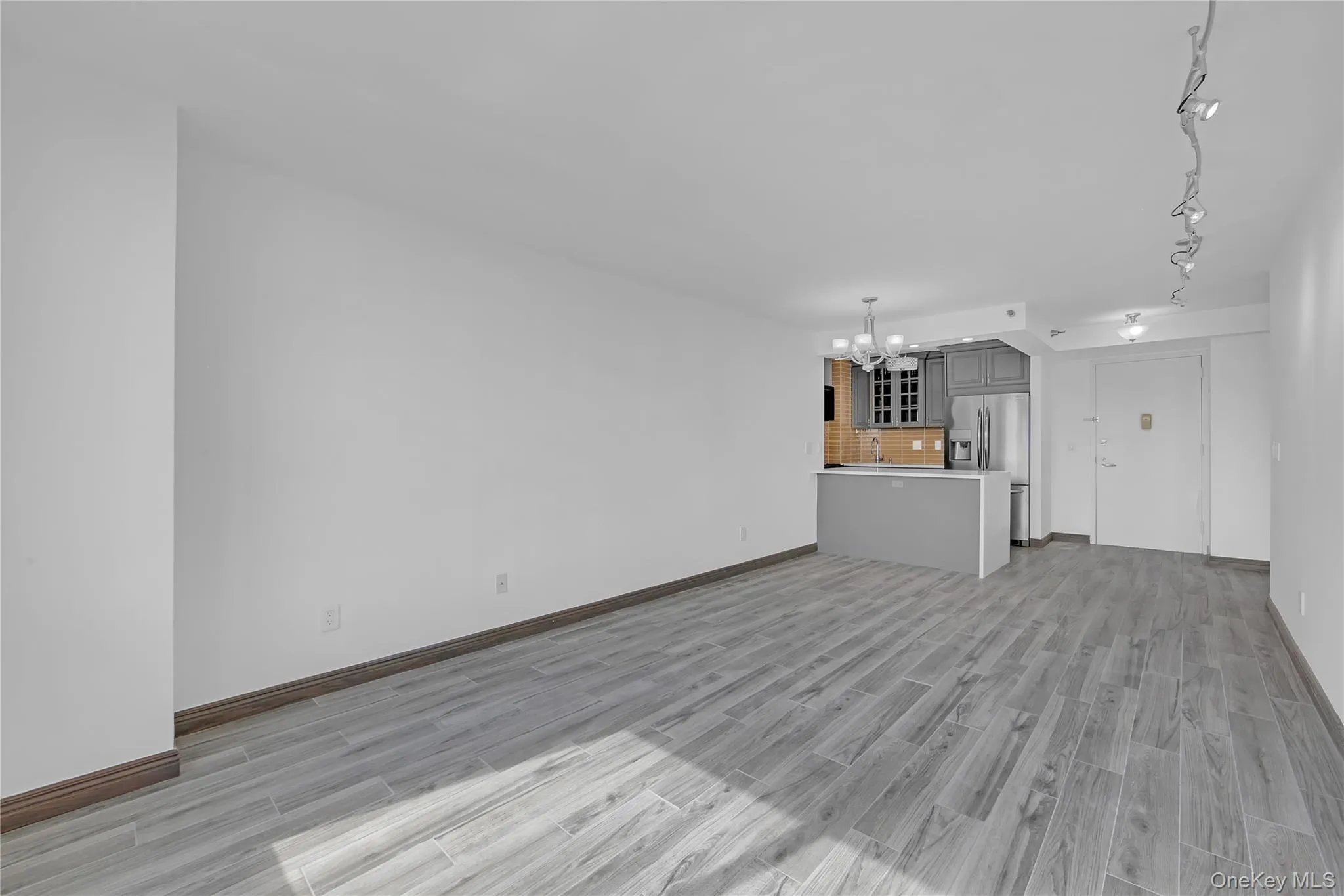 Unfurnished living room with a chandelier, light wood-style flooring, and track lighting Unfurnished living room with a chandelier, light wood-style flooring, and track lighting