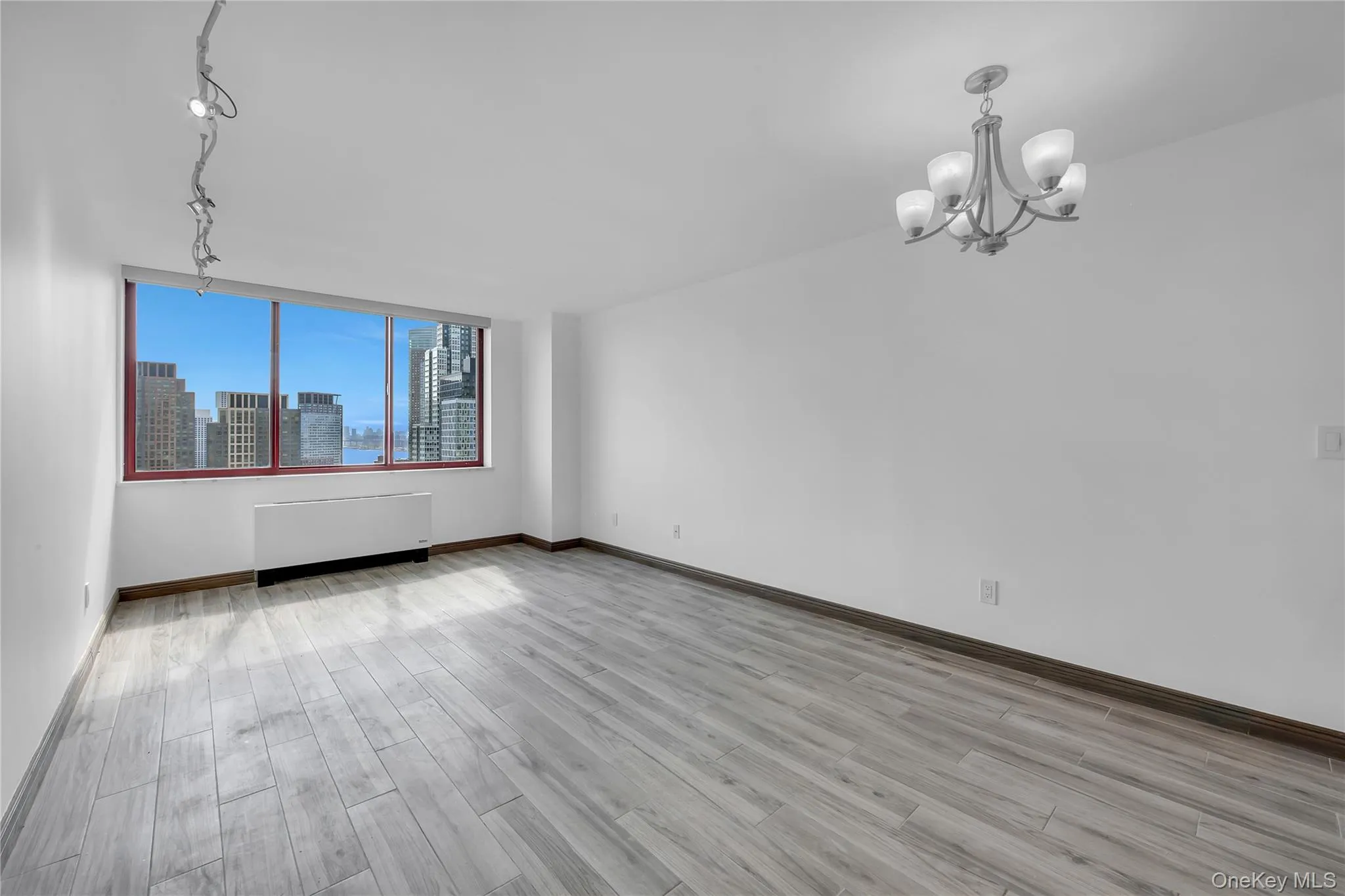 Unfurnished room with a view of skyline, light wood-type flooring, radiator, a chandelier, and track lighting Unfurnished room with a view of skyline, light wood-type flooring, radiator, a chandelier, and track lighting