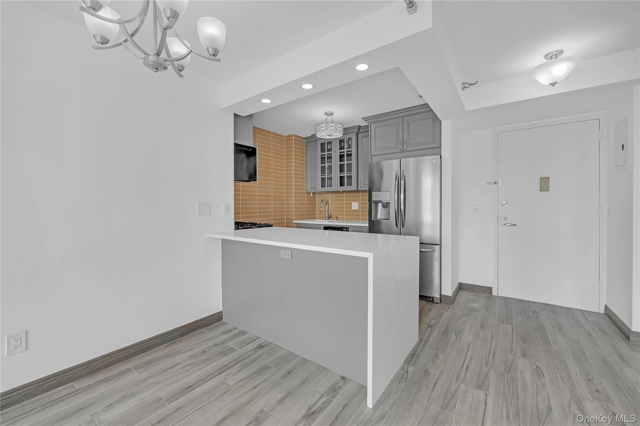 Kitchen featuring a peninsula, gray cabinets, tasteful backsplash, glass insert cabinets, and stainless steel fridge with ice dispenser Kitchen featuring a peninsula, gray cabinets, tasteful backsplash, glass insert cabinets, and stainless steel fridge with ice dispenser
