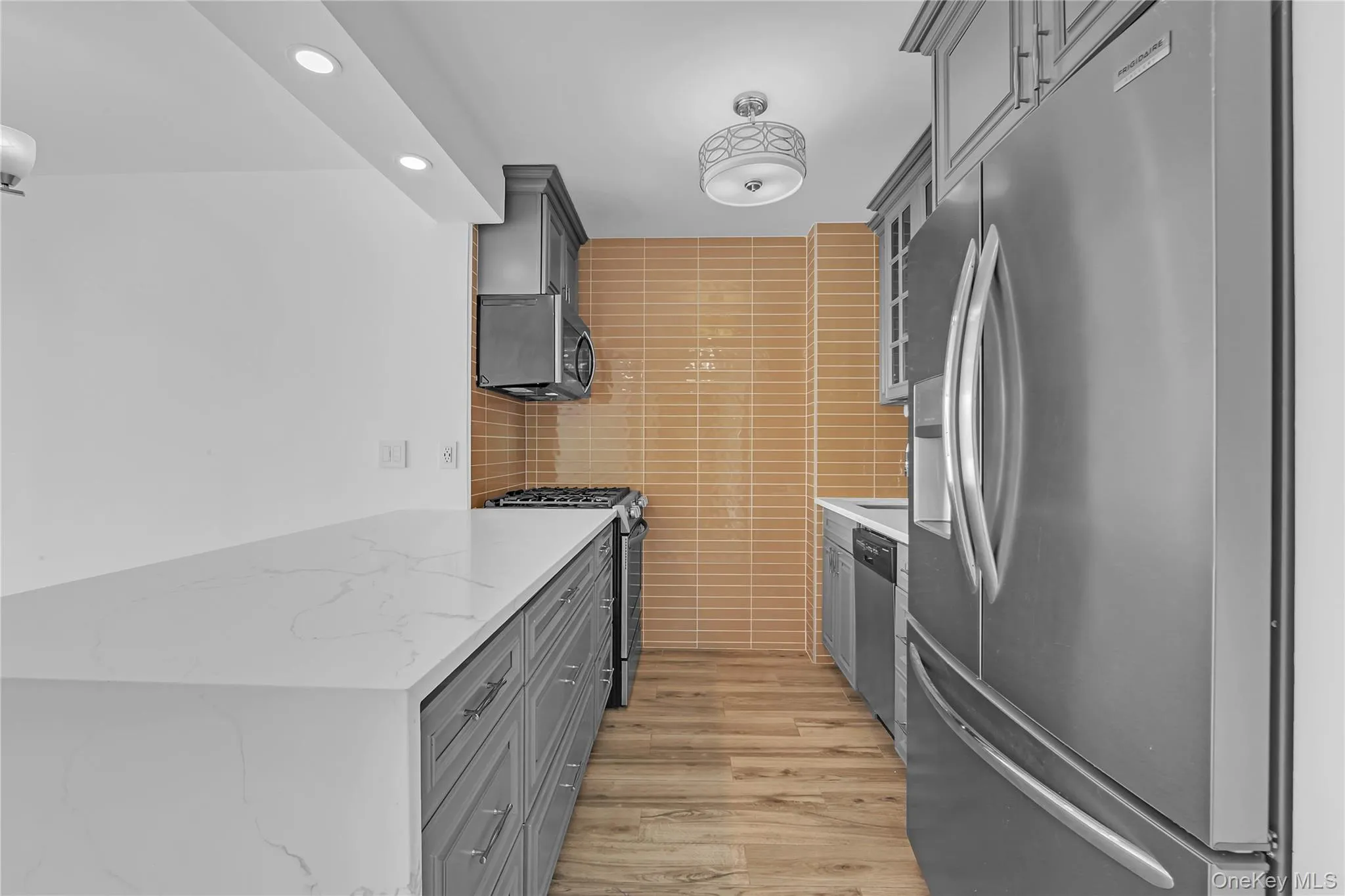 Kitchen with gray cabinetry, stainless steel appliances, light wood-type flooring, recessed lighting, and light stone counters Kitchen with gray cabinetry, stainless steel appliances, light wood-type flooring, recessed lighting, and light stone counters