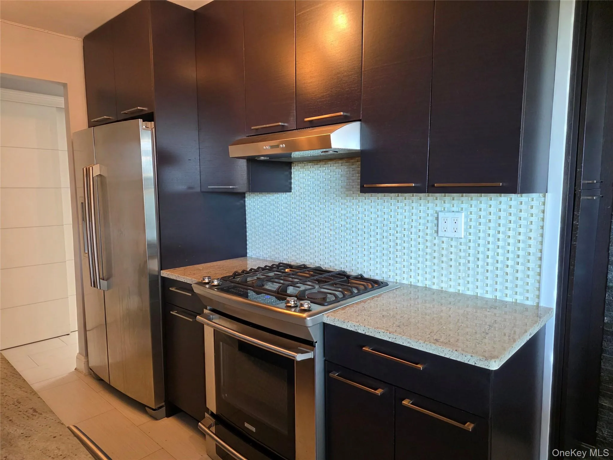 Kitchen with appliances with stainless steel finishes, tasteful backsplash, light stone counters, and under cabinet range hood Kitchen with appliances with stainless steel finishes, tasteful backsplash, light stone counters, and under cabinet range hood