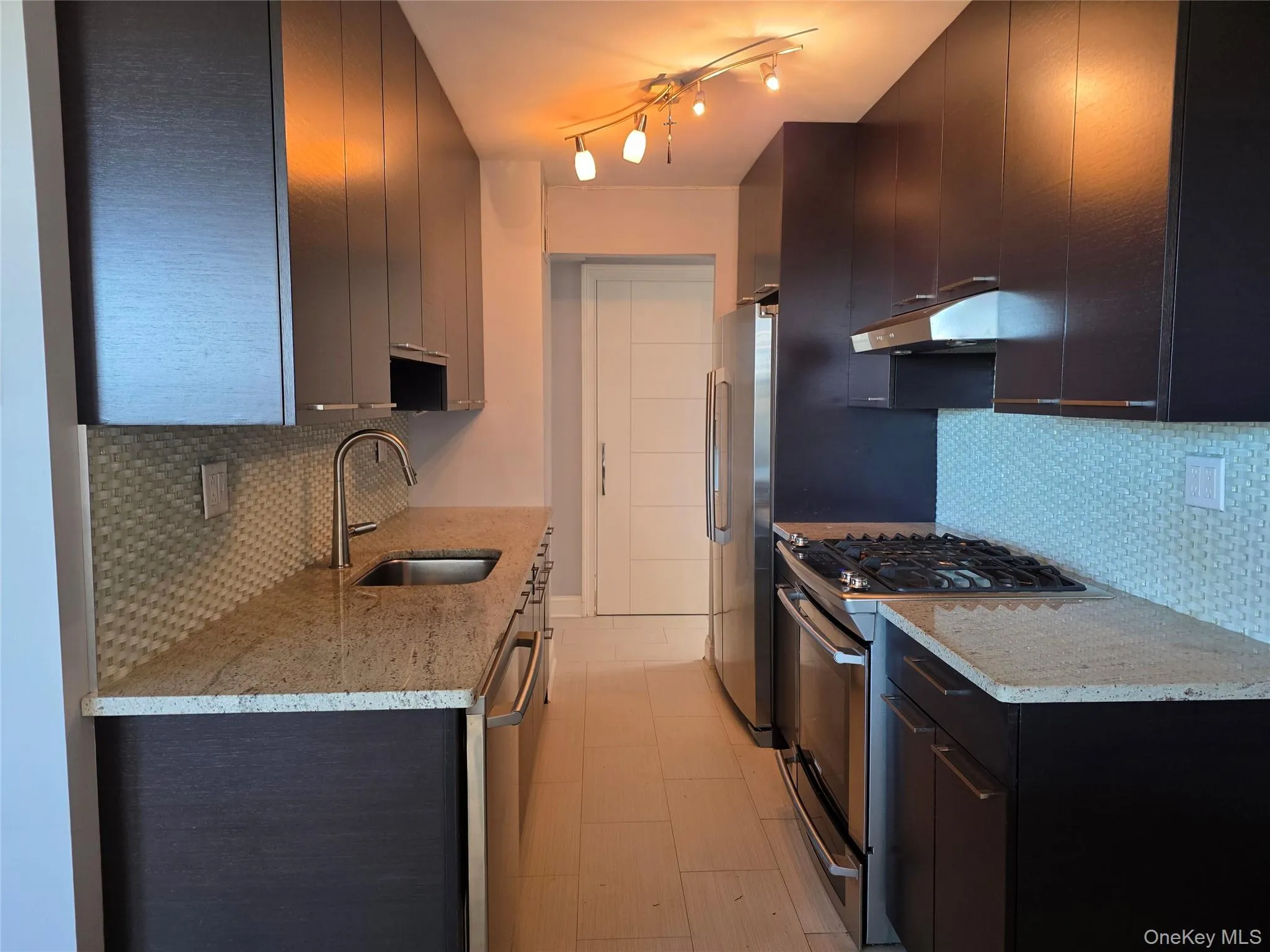 Kitchen featuring tasteful backsplash, appliances with stainless steel finishes, dark cabinets, and light stone counters Kitchen featuring tasteful backsplash, appliances with stainless steel finishes, dark cabinets, and light stone counters