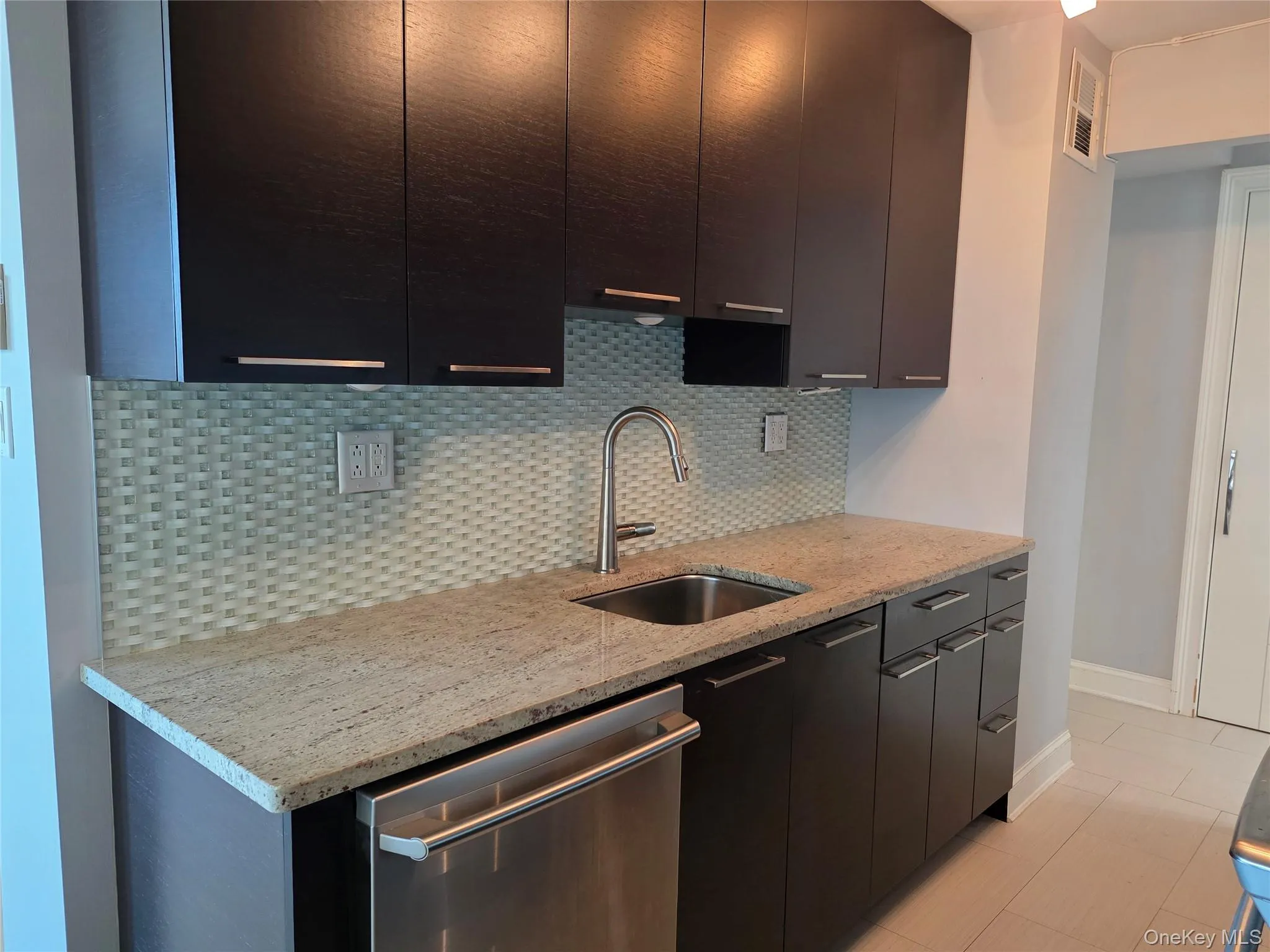 Kitchen with modern cabinets, stainless steel dishwasher, decorative backsplash, light stone counters, and dark cabinets Kitchen with modern cabinets, stainless steel dishwasher, decorative backsplash, light stone counters, and dark cabinets