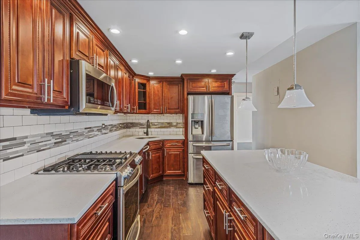 Kitchen featuring appliances with stainless steel finishes, dark wood-style flooring, tasteful backsplash, light stone counters, and recessed lighting Kitchen featuring appliances with stainless steel finishes, dark wood-style flooring, tasteful backsplash, light stone counters, and recessed lighting