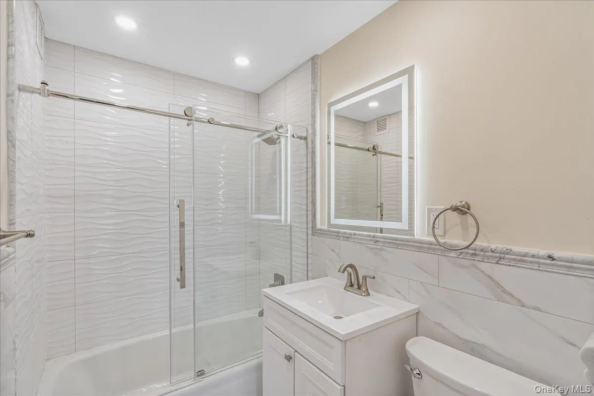 Bathroom with tile walls, bath / shower combo with glass door, and vanity Bathroom with tile walls, bath / shower combo with glass door, and vanity