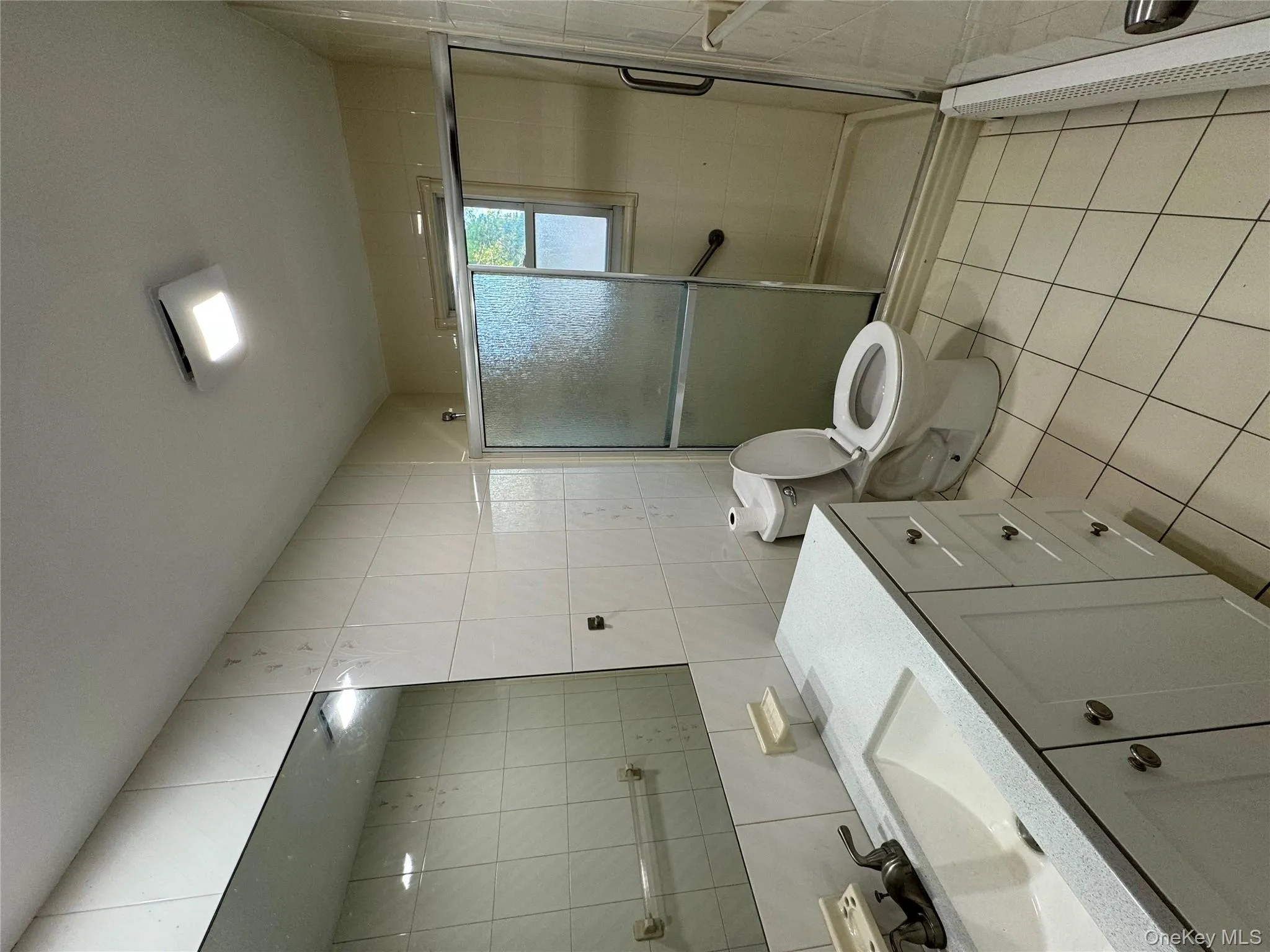 Bathroom with tile walls, vanity, light tile patterned floors, a stall shower, and a baseboard heating unit Bathroom with tile walls, vanity, light tile patterned floors, a stall shower, and a baseboard heating unit