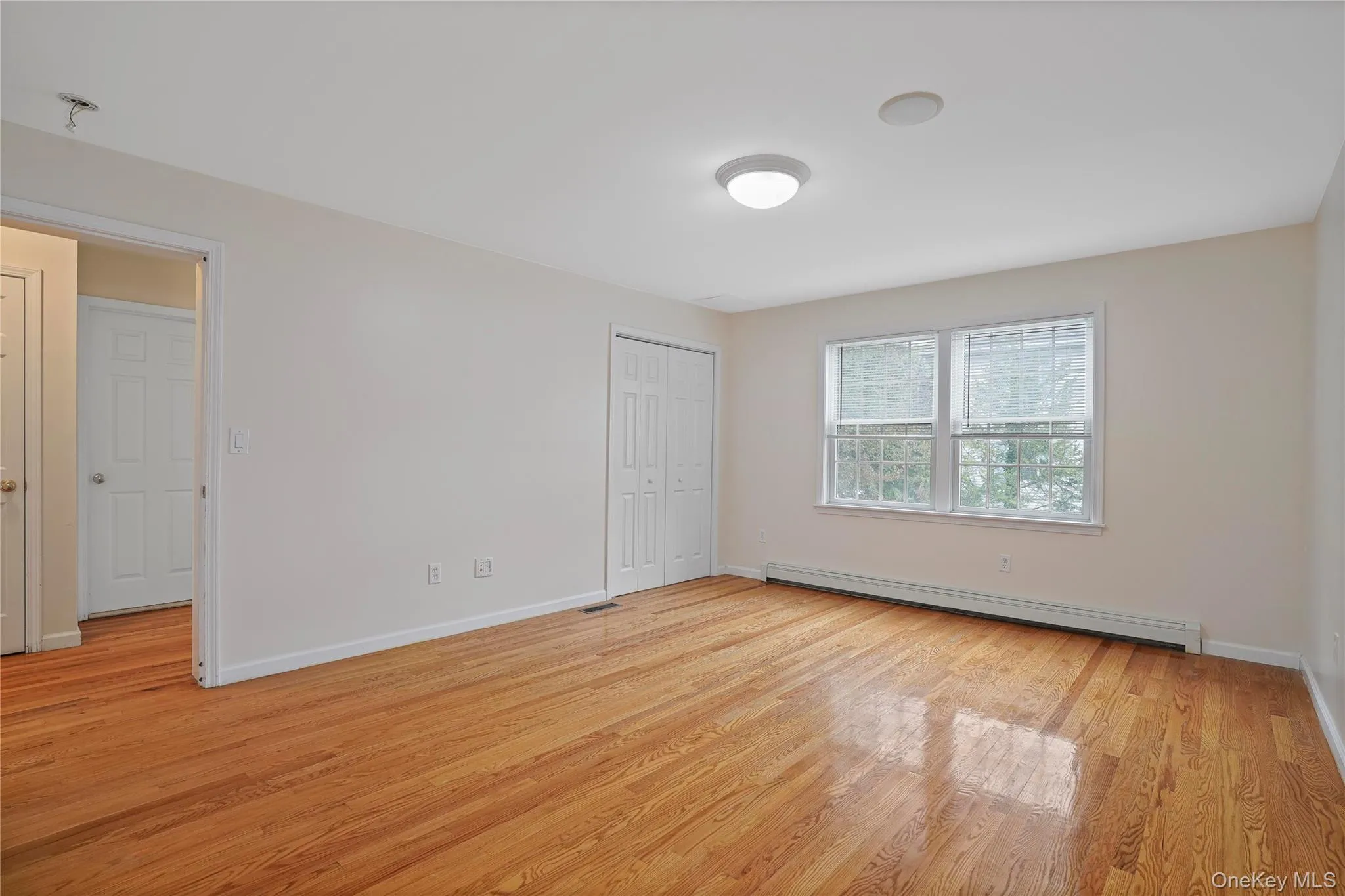 Unfurnished bedroom with baseboard heating, light wood-type flooring, and a closet Unfurnished bedroom with baseboard heating, light wood-type flooring, and a closet
