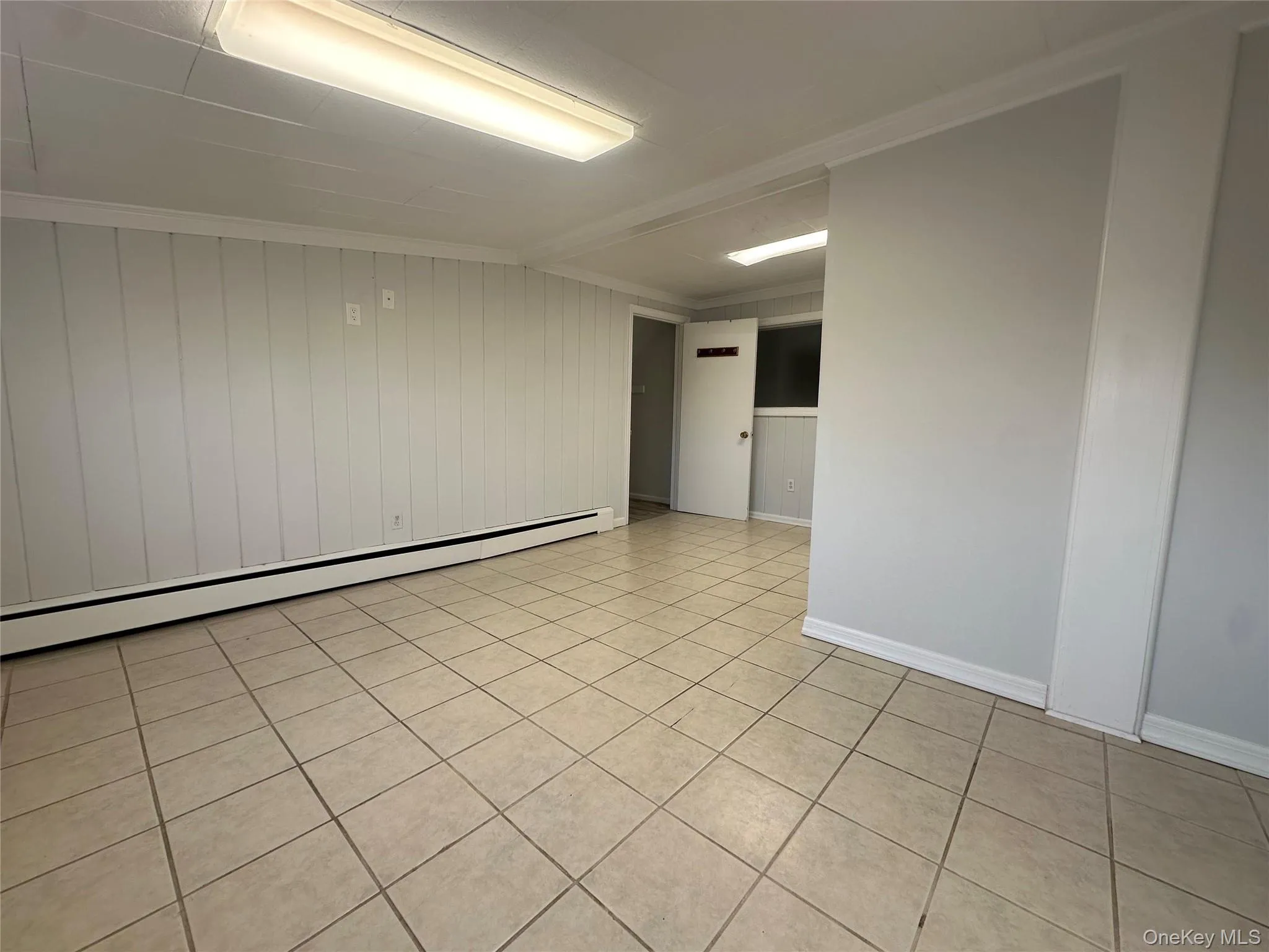 Empty room featuring a baseboard radiator, ornamental molding, and light tile patterned floors Empty room featuring a baseboard radiator, ornamental molding, and light tile patterned floors