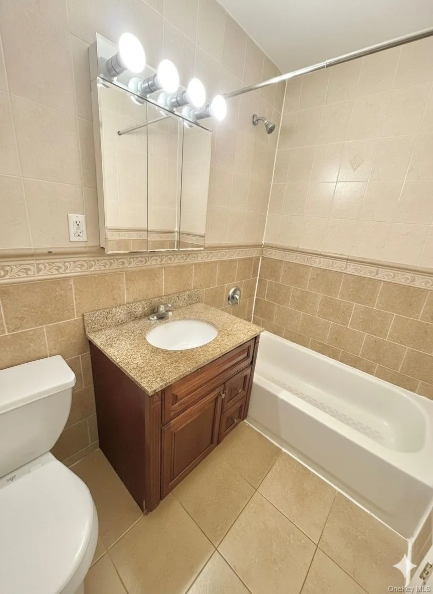 Bathroom featuring tile walls, bathing tub / shower combination, light tile patterned floors, and vanity Bathroom featuring tile walls, bathing tub / shower combination, light tile patterned floors, and vanity