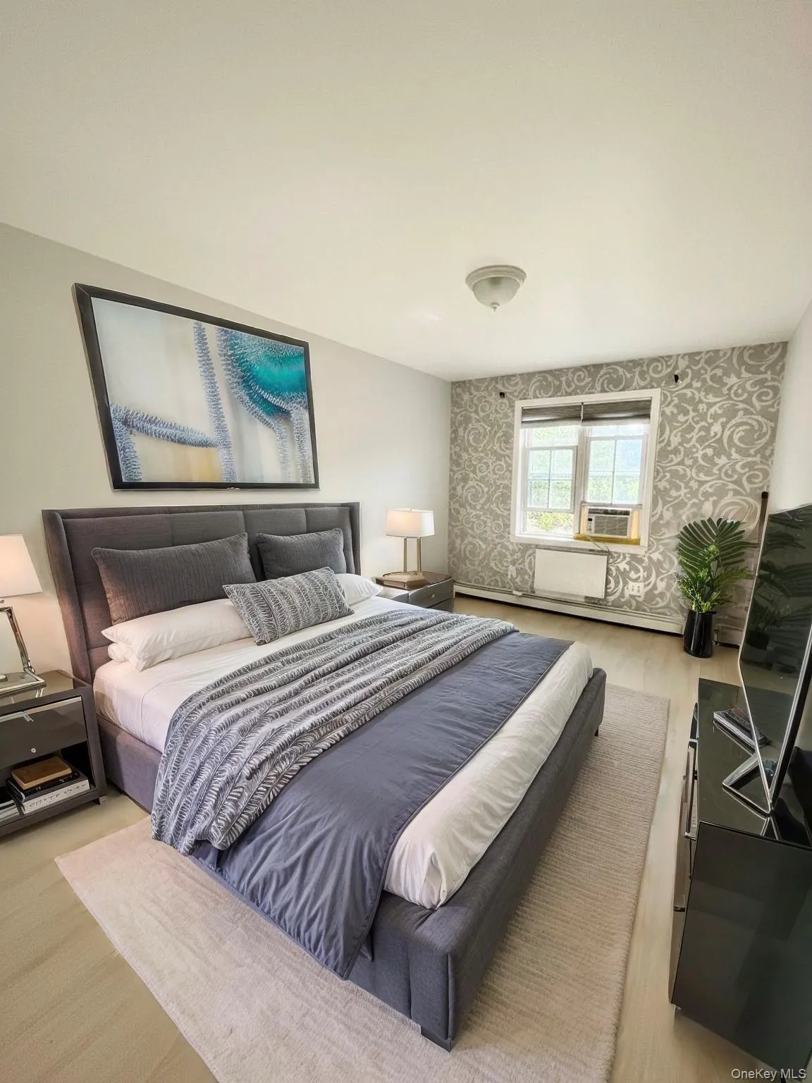 Bedroom featuring baseboard heating, wallpapered walls, light wood finished floors, and cooling unit Bedroom featuring baseboard heating, wallpapered walls, light wood finished floors, and cooling unit