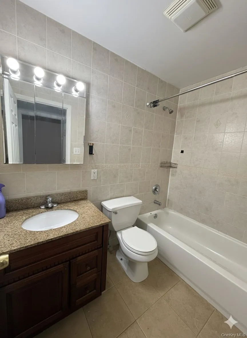 Bathroom featuring tile walls, vanity, bathing tub / shower combination, decorative backsplash, and light tile patterned floors Bathroom featuring tile walls, vanity, bathing tub / shower combination, decorative backsplash, and light tile patterned floors