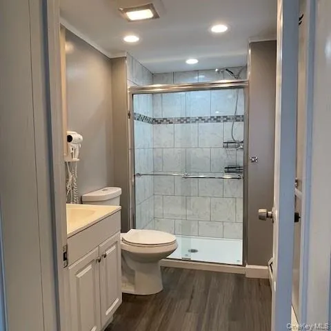 Primary bathroom offers linen closet, vanity, mirror, attached hair drier, tiled shower, window, wood floor, baseboard and recessed lighting Primary bathroom offers linen closet, vanity, mirror, attached hair drier, tiled shower, window, wood floor, baseboard and recessed lighting