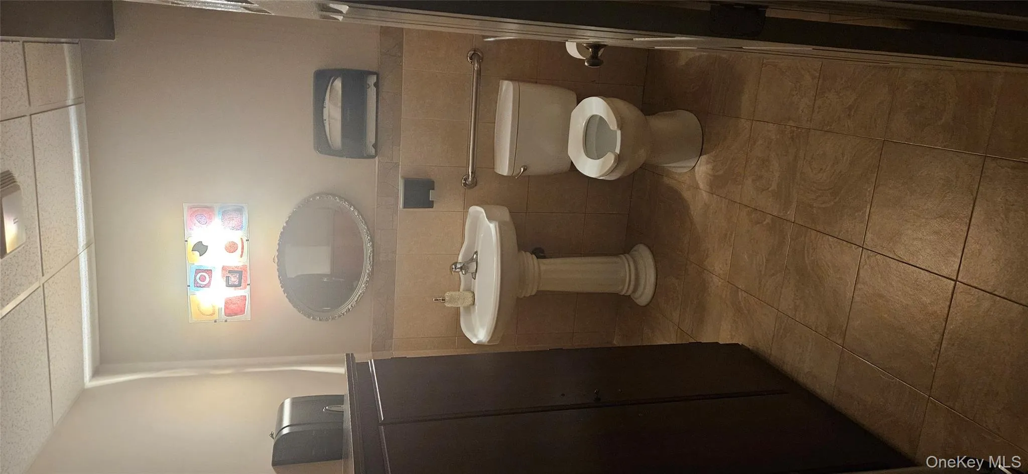 Half bathroom featuring tile walls, dark tile patterned flooring, a drop ceiling, and a wainscoted wall Half bathroom featuring tile walls, dark tile patterned flooring, a drop ceiling, and a wainscoted wall