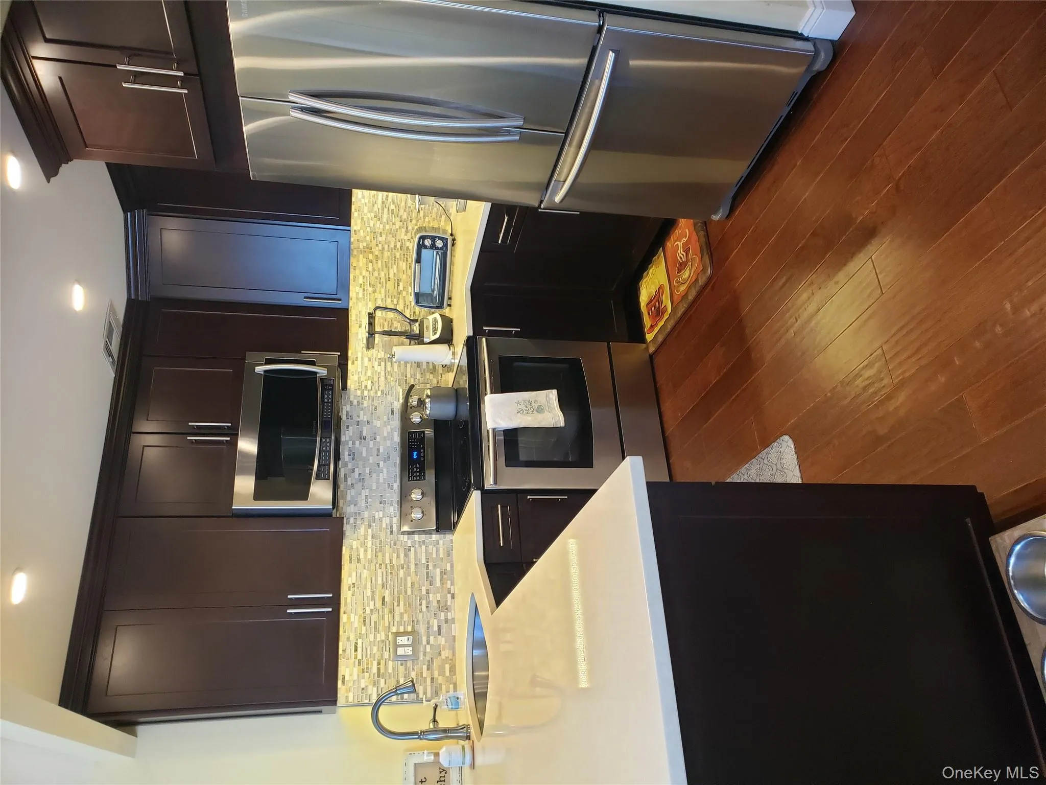 Kitchen with stainless steel appliances, light stone countertops, dark wood finished floors, tasteful backsplash, and dark brown cabinets Kitchen with stainless steel appliances, light stone countertops, dark wood finished floors, tasteful backsplash, and dark brown cabinets