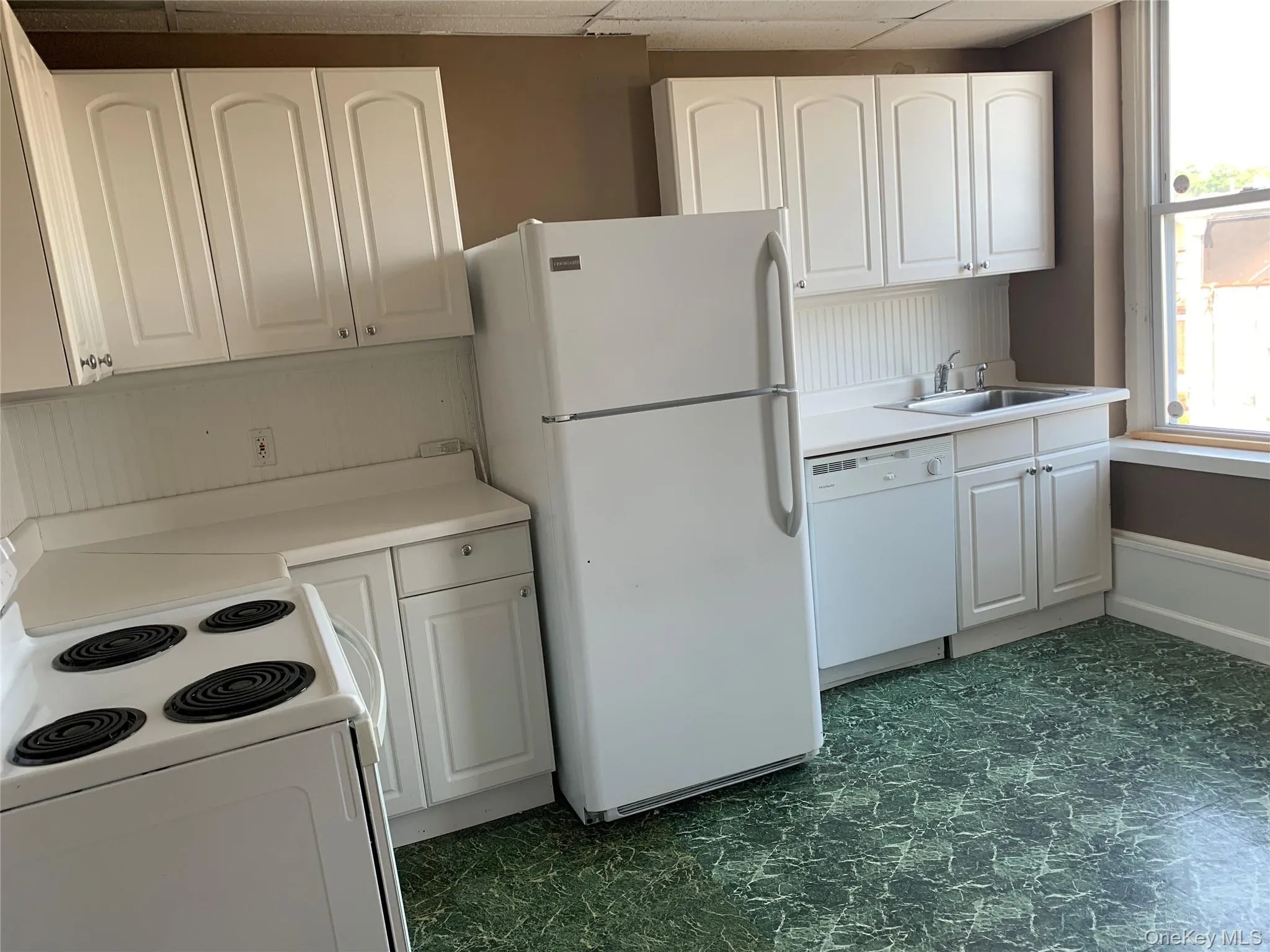 Kitchen with white appliances, white cabinetry, light countertops, and a drop ceiling Kitchen with white appliances, white cabinetry, light countertops, and a drop ceiling