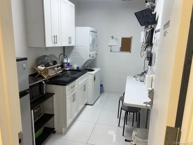 Kitchen featuring stacked washer and clothes dryer, white cabinets, dark countertops, light tile patterned floors, and appliances with stainless steel finishes Kitchen featuring stacked washer and clothes dryer, white cabinets, dark countertops, light tile patterned floors, and appliances with stainless steel finishes