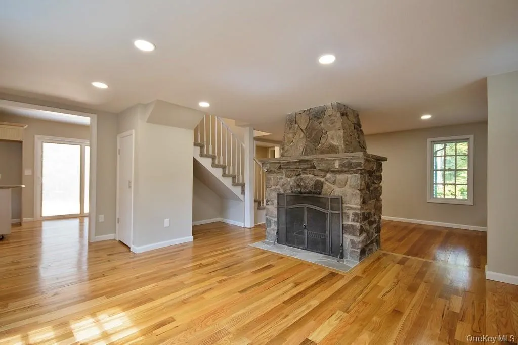 Unfurnished living room featuring light wood finished floors, a stone fireplace, recessed lighting, and stairs Unfurnished living room featuring light wood finished floors, a stone fireplace, recessed lighting, and stairs