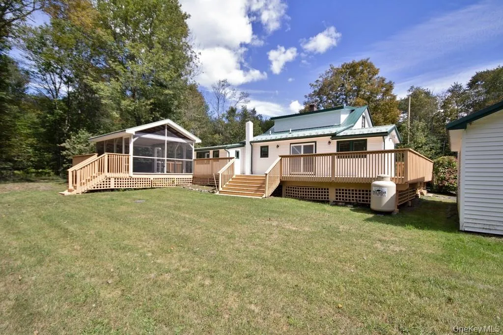 Back of property featuring a sunroom, a deck, and a lawn Back of property featuring a sunroom, a deck, and a lawn