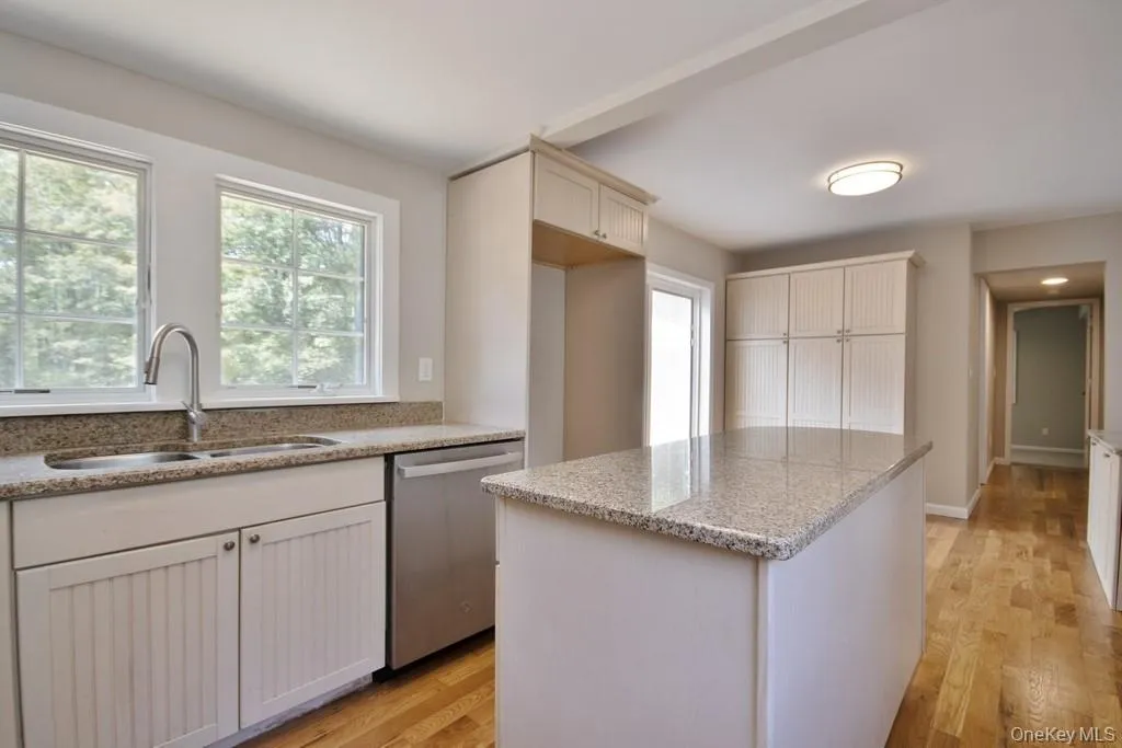 Kitchen featuring light wood-style flooring, a center island, stainless steel dishwasher, and light stone counters Kitchen featuring light wood-style flooring, a center island, stainless steel dishwasher, and light stone counters