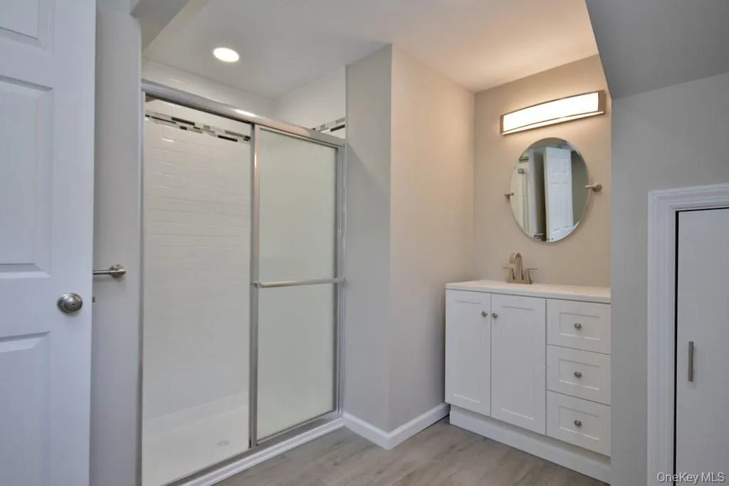 Full bath with a stall shower, vanity, light wood-style flooring, and recessed lighting Full bath with a stall shower, vanity, light wood-style flooring, and recessed lighting