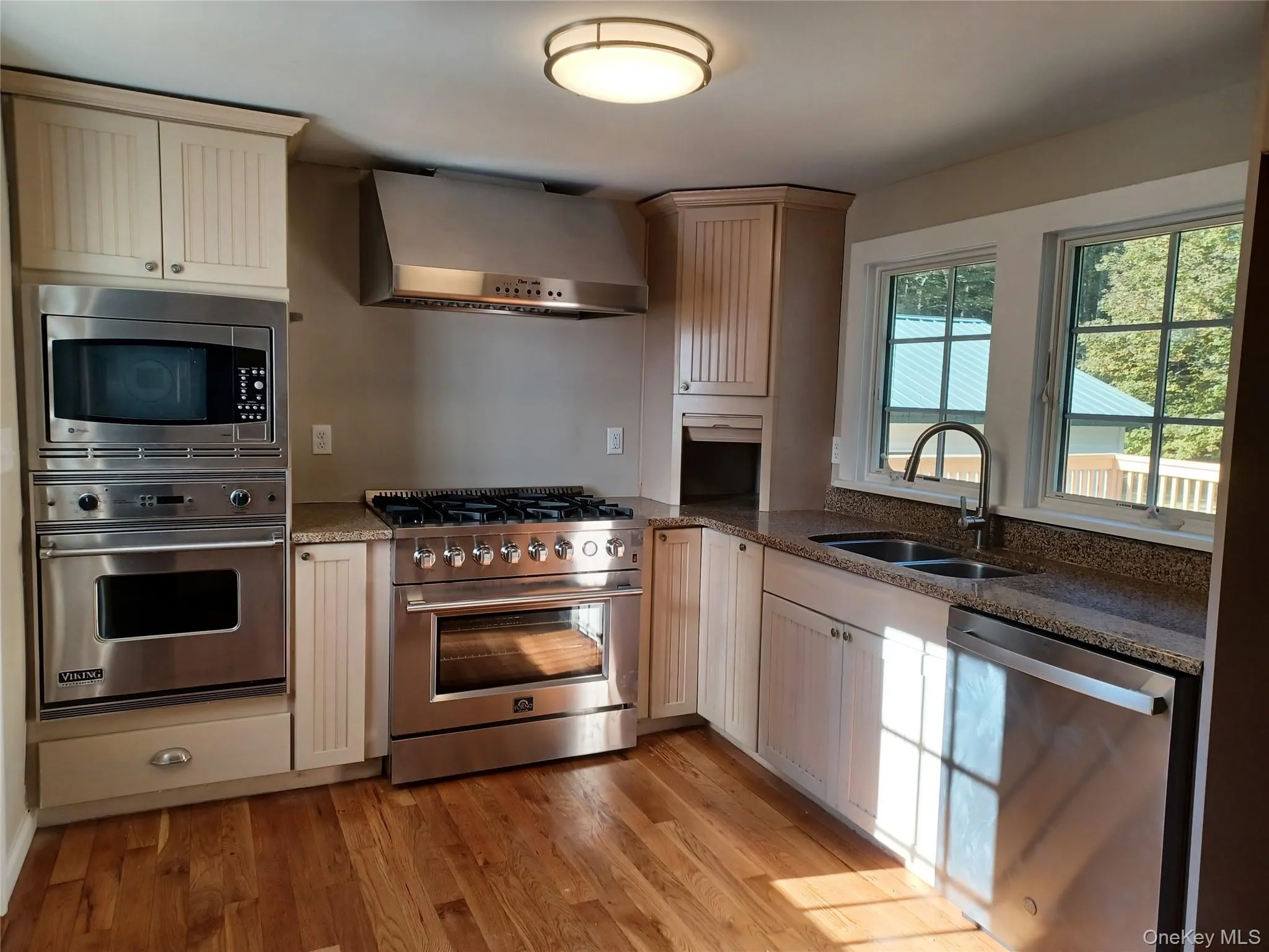 Kitchen with stainless steel appliances, extractor fan, dark stone counters, and light wood-style floors Kitchen with stainless steel appliances, extractor fan, dark stone counters, and light wood-style floors