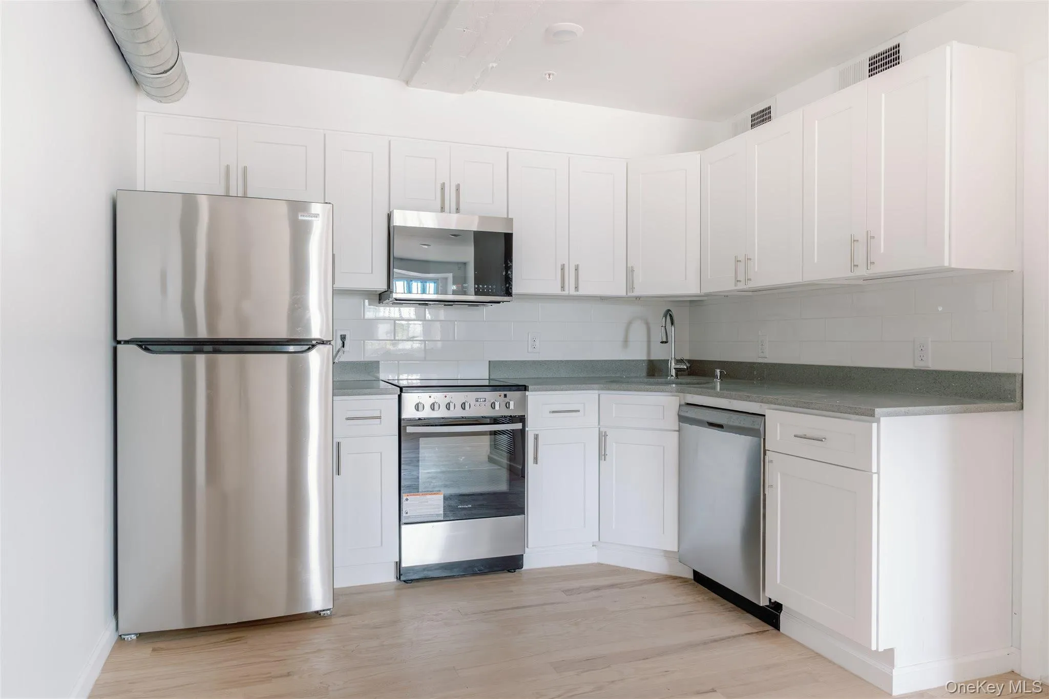 Kitchen with appliances with stainless steel finishes, white cabinets, decorative backsplash, light wood-style floors, and dark stone countertops Kitchen with appliances with stainless steel finishes, white cabinets, decorative backsplash, light wood-style floors, and dark stone countertops