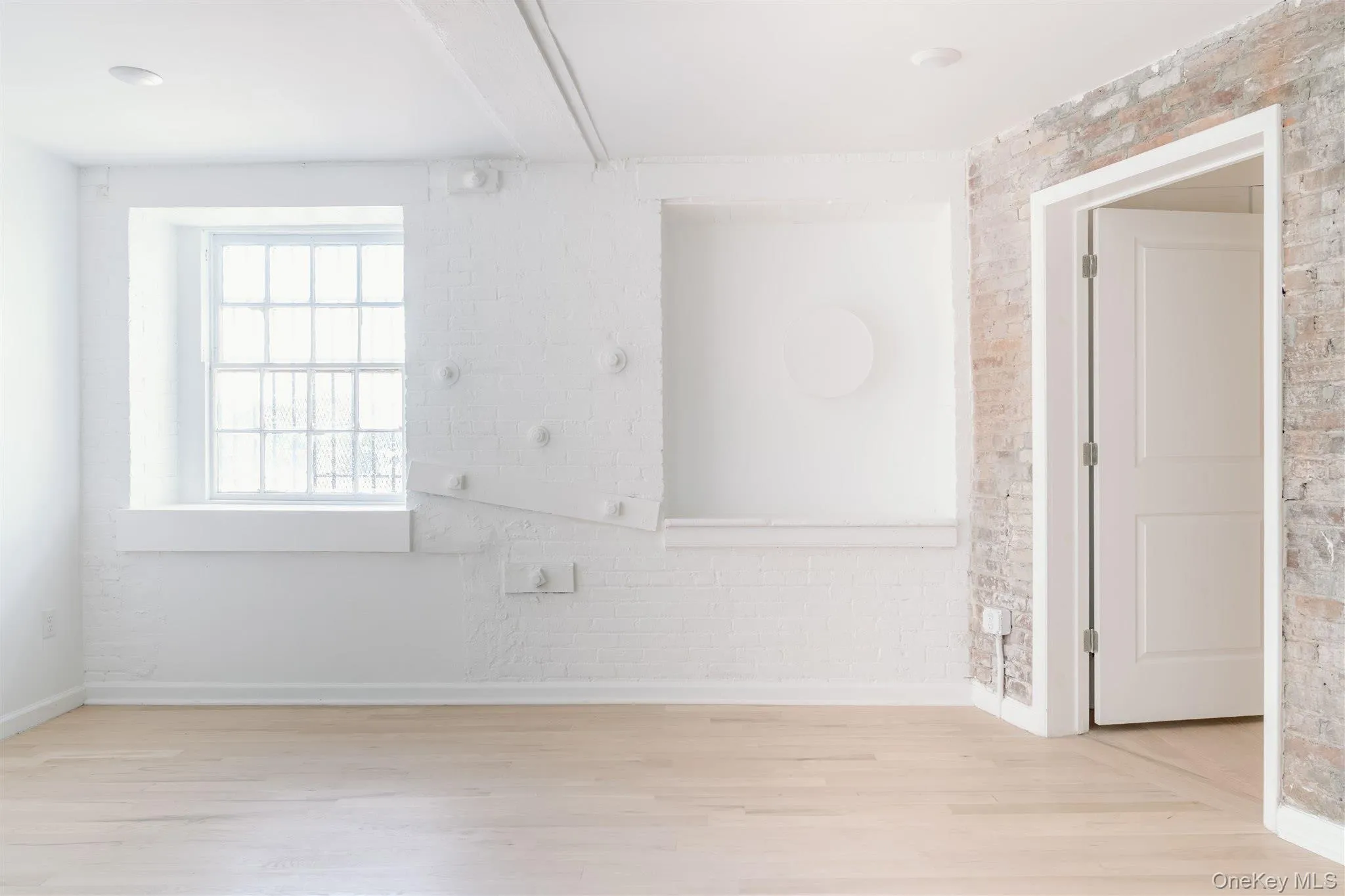 Spare room featuring brick wall and light wood-style floors Spare room featuring brick wall and light wood-style floors