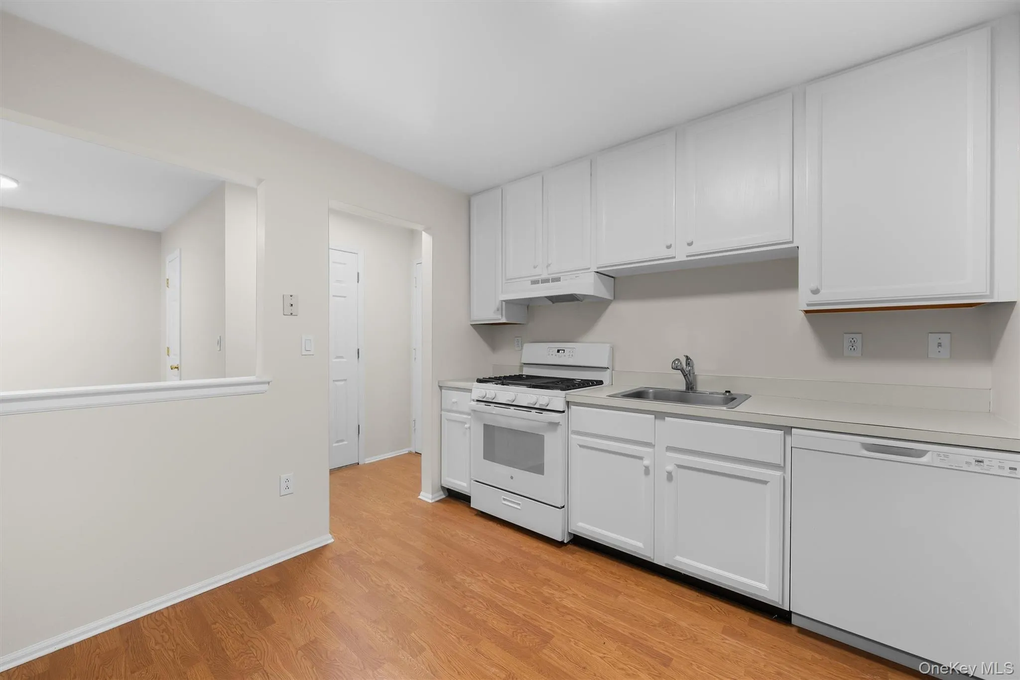 Kitchen featuring white appliances, light wood-style flooring, under cabinet range hood, a sink, and white cabinetry Kitchen featuring white appliances, light wood-style flooring, under cabinet range hood, a sink, and white cabinetry