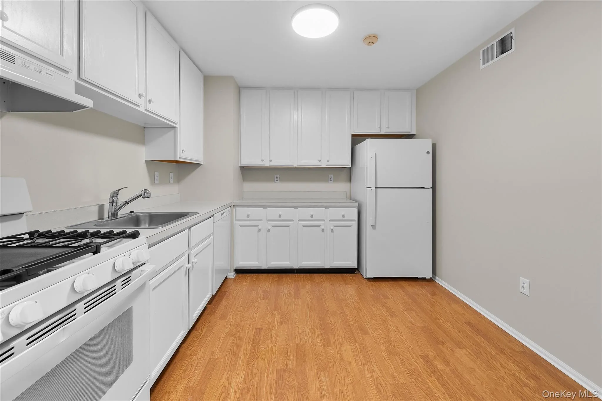 Kitchen with white appliances, extractor fan, light wood finished floors, a sink, and visible vents Kitchen with white appliances, extractor fan, light wood finished floors, a sink, and visible vents