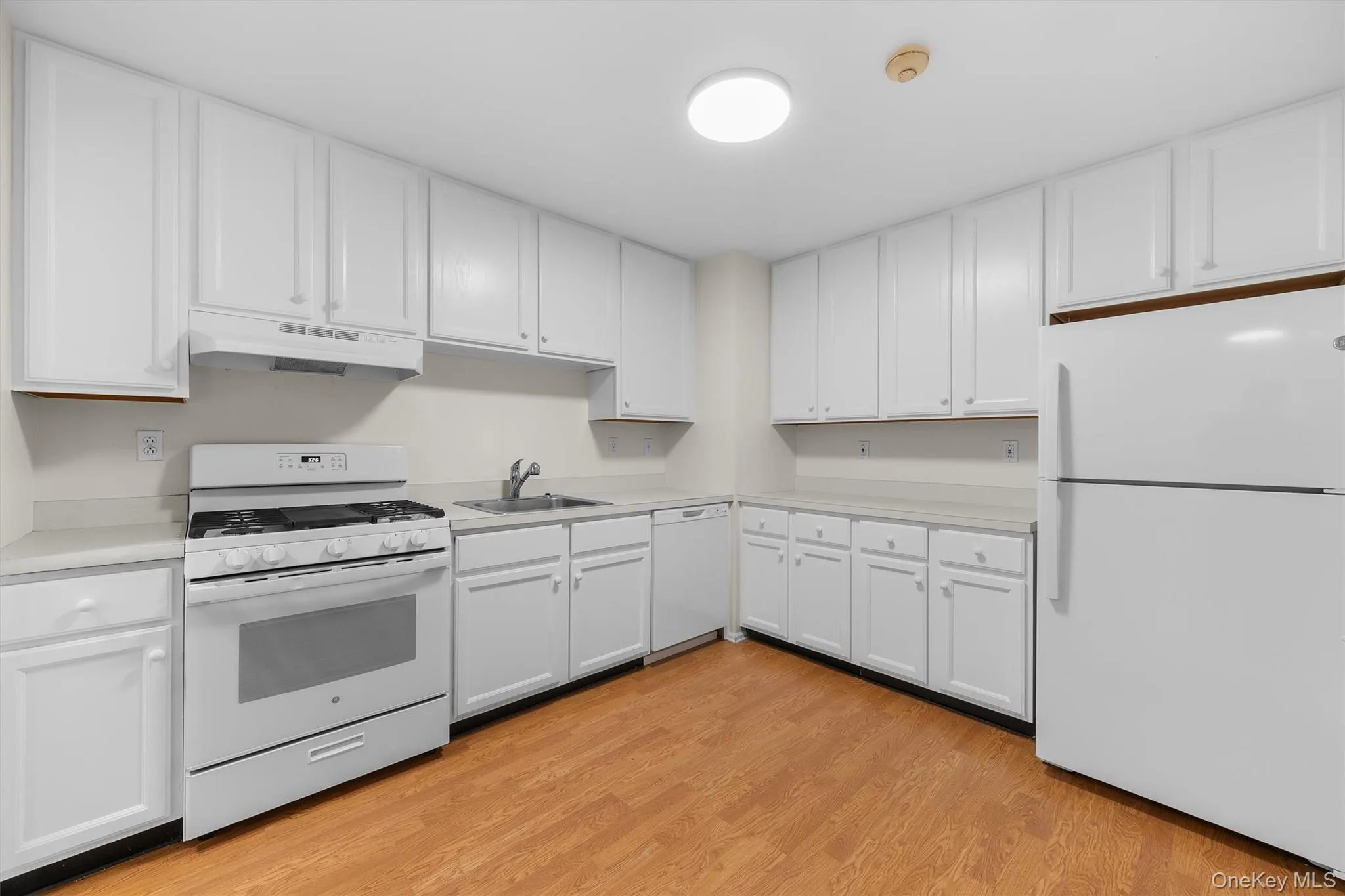 Kitchen featuring white appliances, under cabinet range hood, light countertops, white cabinets, and a sink Kitchen featuring white appliances, under cabinet range hood, light countertops, white cabinets, and a sink