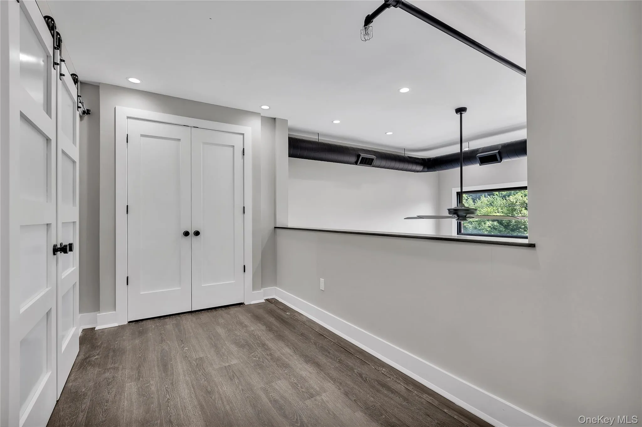 Empty room featuring a barn door, wood finished floors, and recessed lighting Empty room featuring a barn door, wood finished floors, and recessed lighting