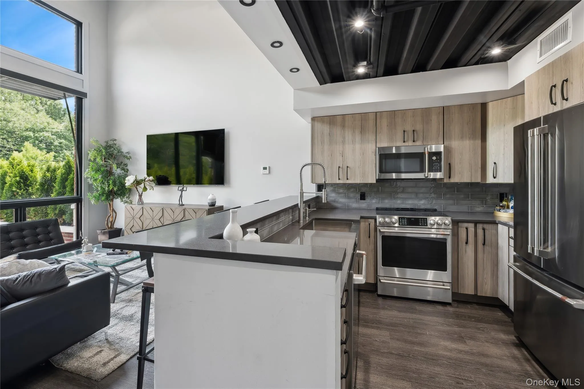 Kitchen featuring stainless steel appliances, a kitchen breakfast bar, a peninsula, tasteful backsplash, and dark wood-style flooring Kitchen featuring stainless steel appliances, a kitchen breakfast bar, a peninsula, tasteful backsplash, and dark wood-style flooring
