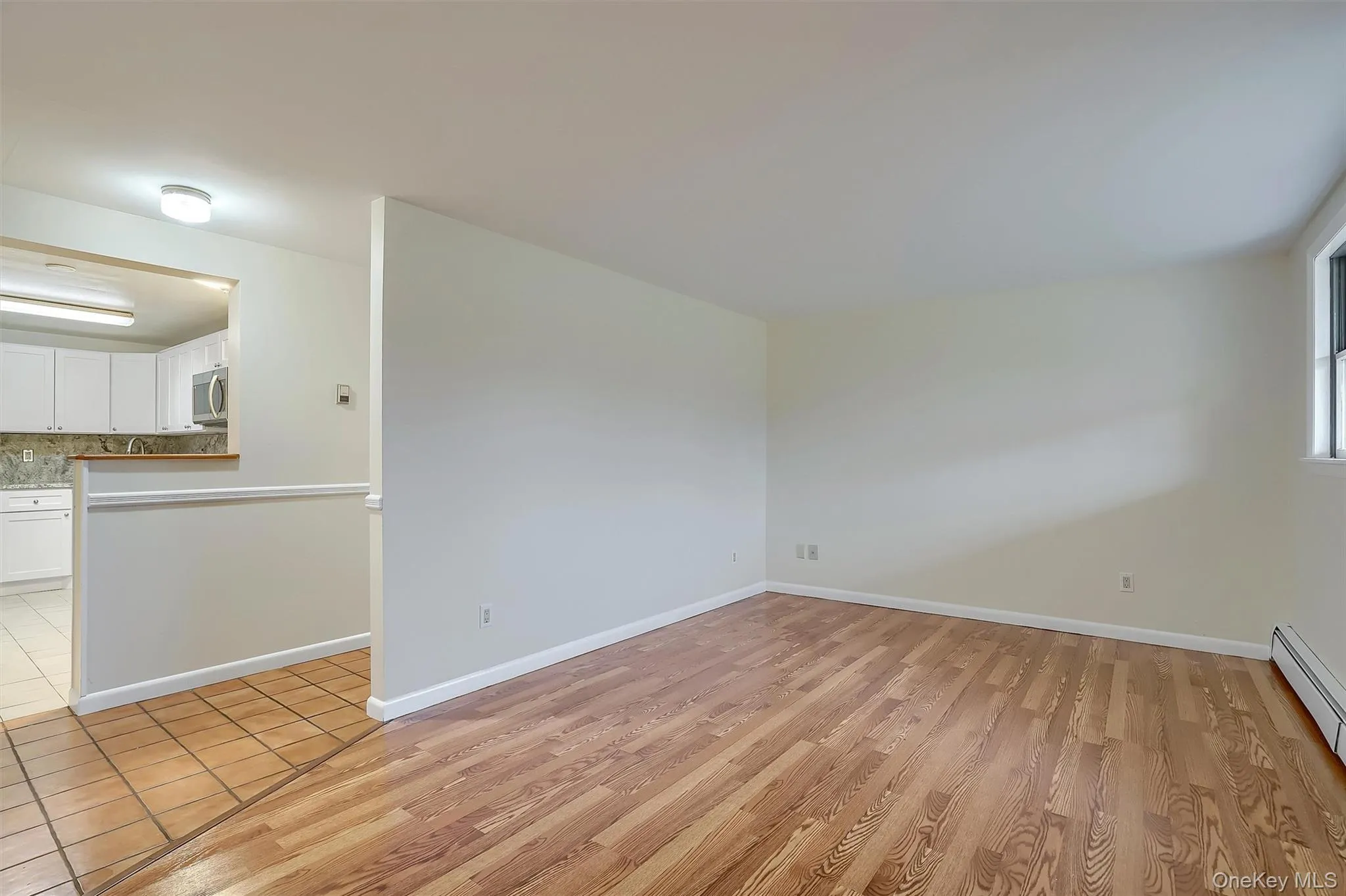 Unfurnished living room featuring light wood-style floors and baseboard heating Unfurnished living room featuring light wood-style floors and baseboard heating