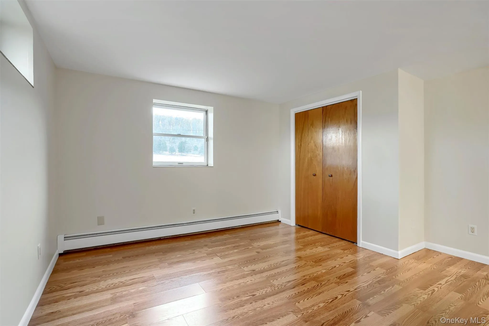 Unfurnished bedroom featuring baseboard heating, light wood finished floors, and a closet Unfurnished bedroom featuring baseboard heating, light wood finished floors, and a closet